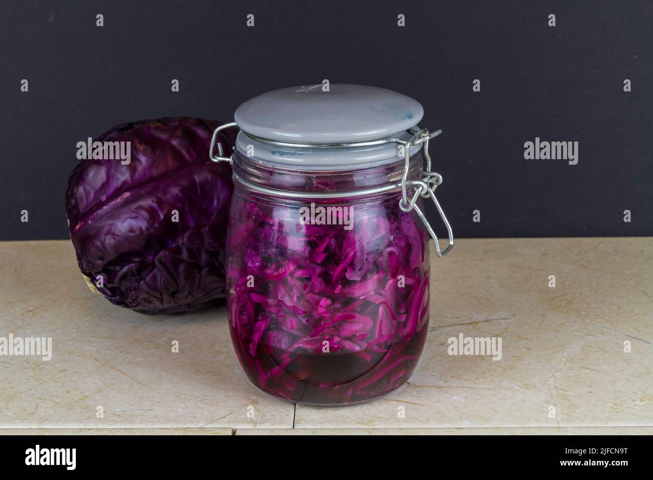 Jar of freshly made sauerkraut with whole red cabbage behind, landscape. Stock Photo