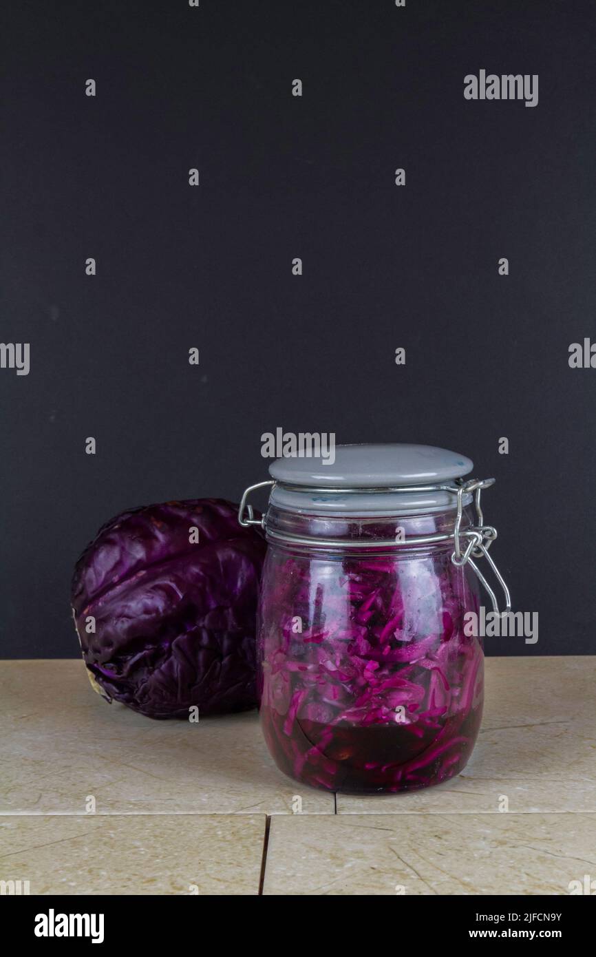 Jar of freshly made sauerkraut with whole red cabbage behind, portrait, dark copyspace at top. Stock Photo