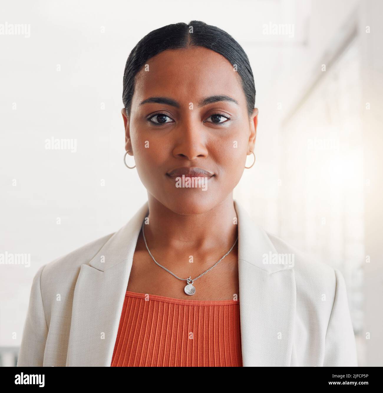 Young mixed race businesswoman standing alone in an office at work. Face of one confident hispanic businessperson looking serious standing at work Stock Photo