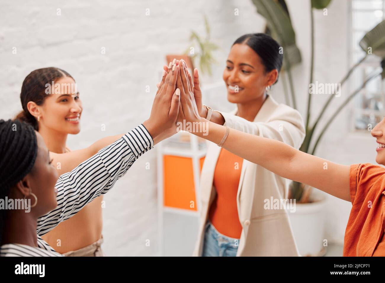 Four happy businesswomen joining their hands together in an office at work. Diverse group of cheerful businesspeople giving each other a high five in Stock Photo