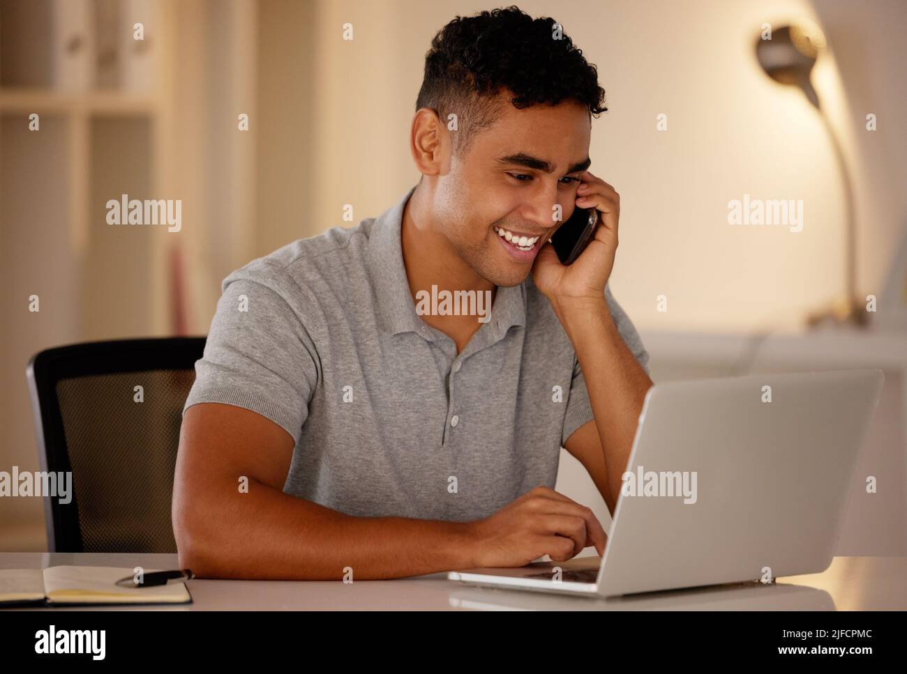 One young mixed race business man multitasking by talking on a cellphone and using a laptop to browse the internet. Happy, ambitious entrepreneur Stock Photo
