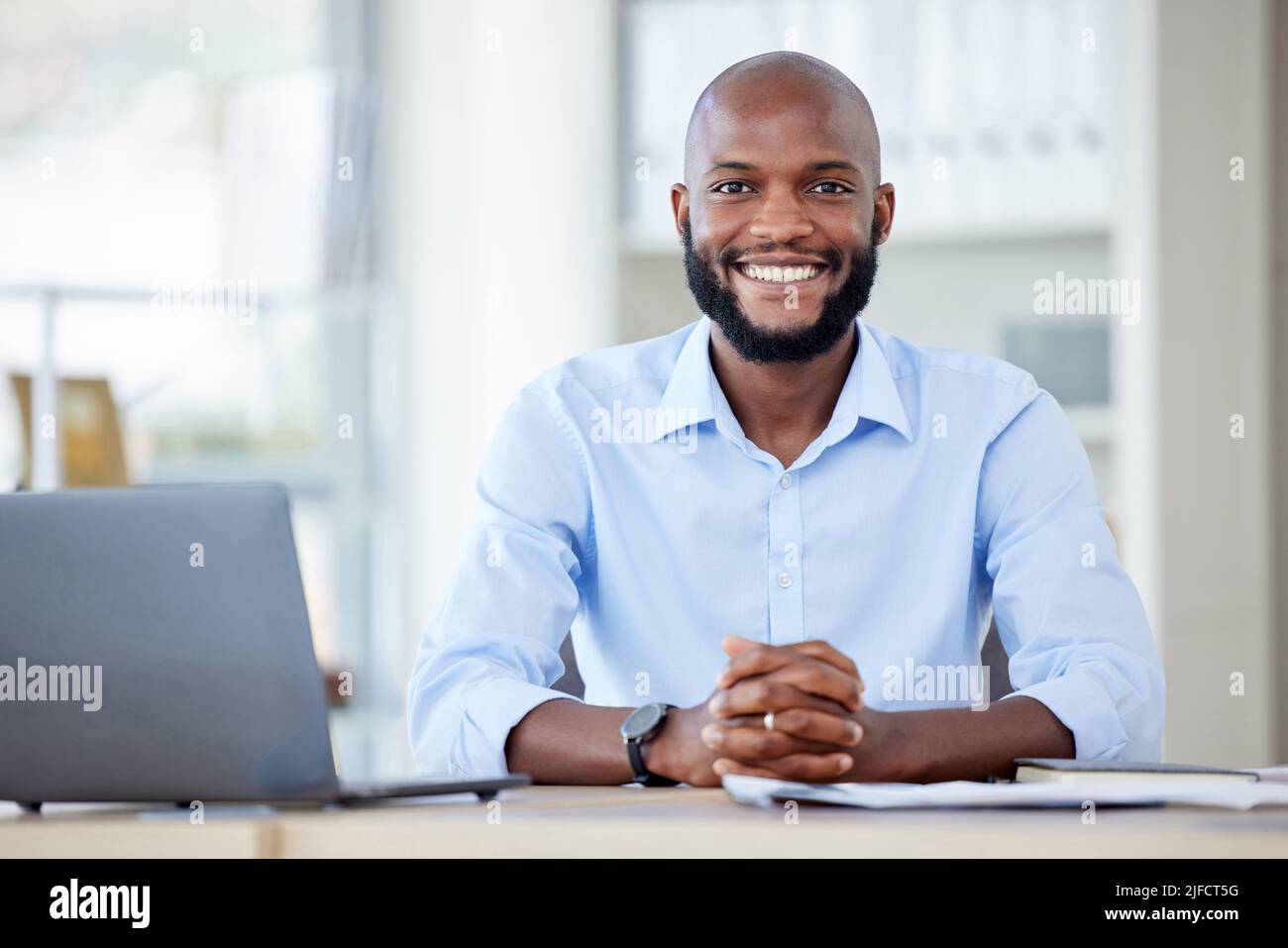 Portrait of a young happy african american businessman sitting at a desk in  an office alone at work. One male businessperson smiling while using a  Stock Photo - Alamy, image size:1300x957