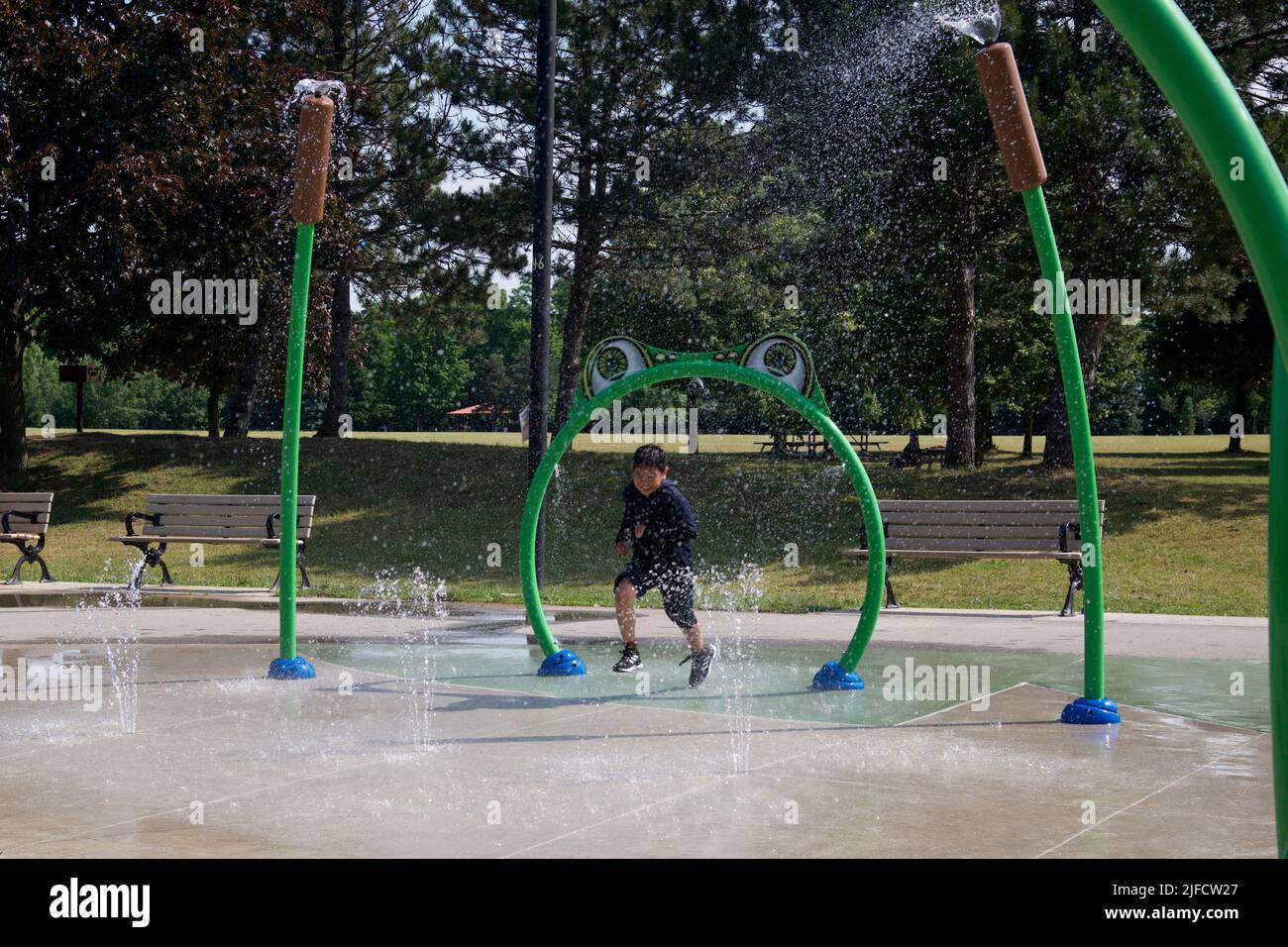 Toronto, Ontario / Canada - 06/30/2022: Happy child has fun playing in water fountains on a hot day during summer. Boy running in the spray park. Stock Photo