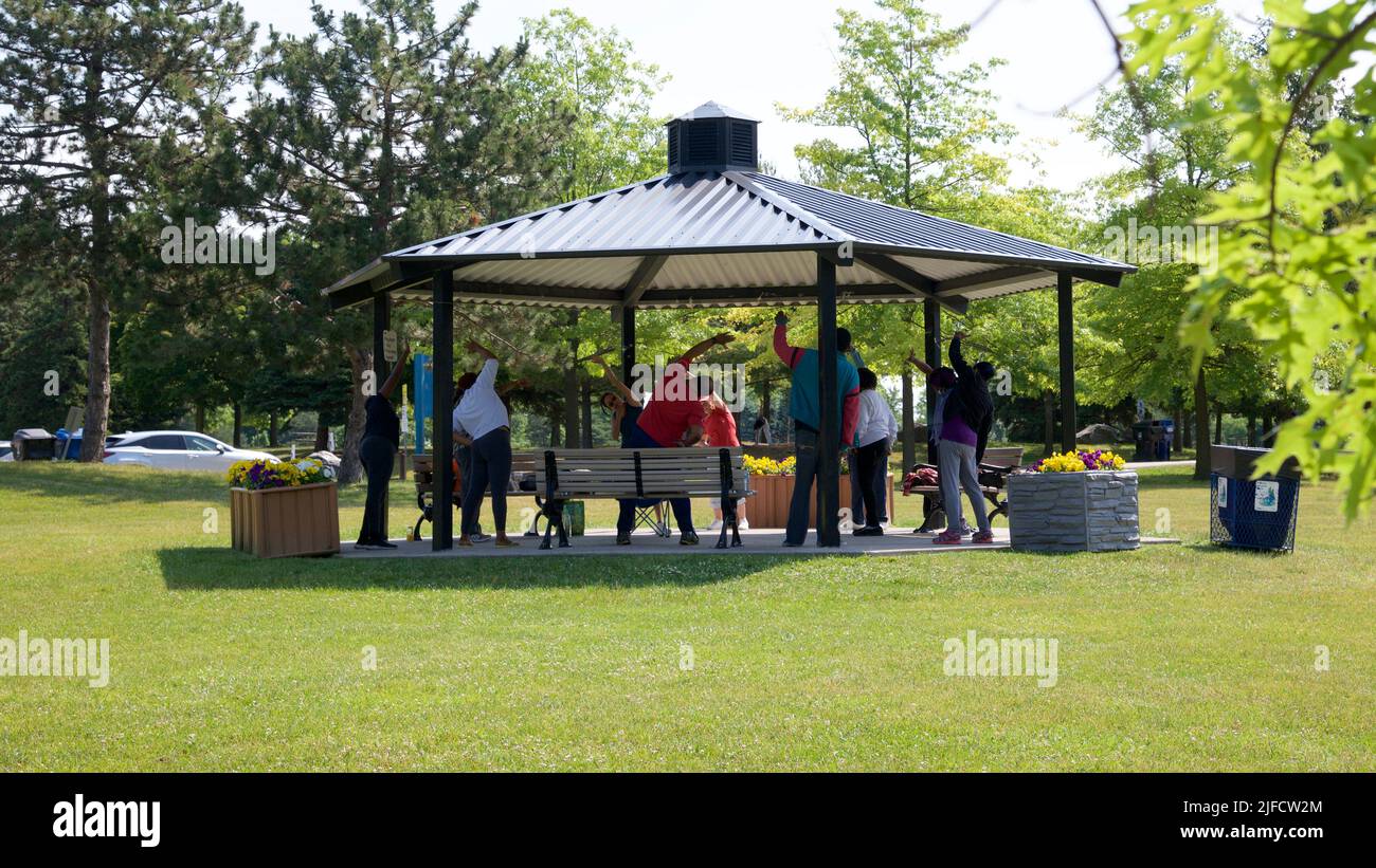 Toronto, Ontario / Canada - 06/30/2022: fitness, sport and healthy lifestyle concept - group of happy people exercising with trainer at summer park  P Stock Photo