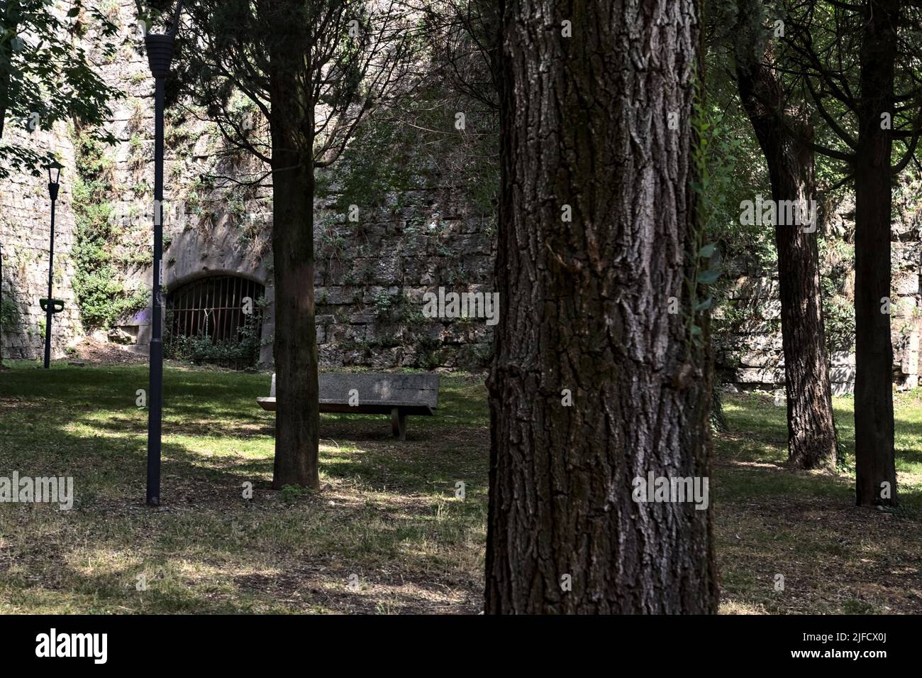 Corner of a fortification in a park with trees and a bench in the shade