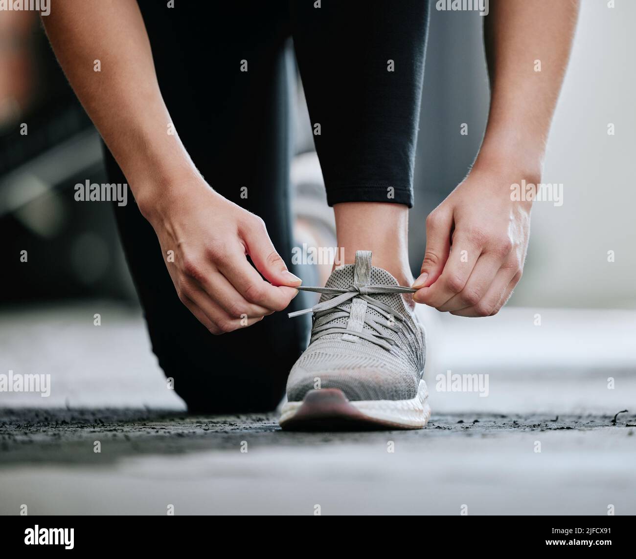 Closeup of unknown trainer tying shoelaces alone in gym. One caucasian coach kneeling, getting ready to workout health club. Woman crouching down in Stock Photo