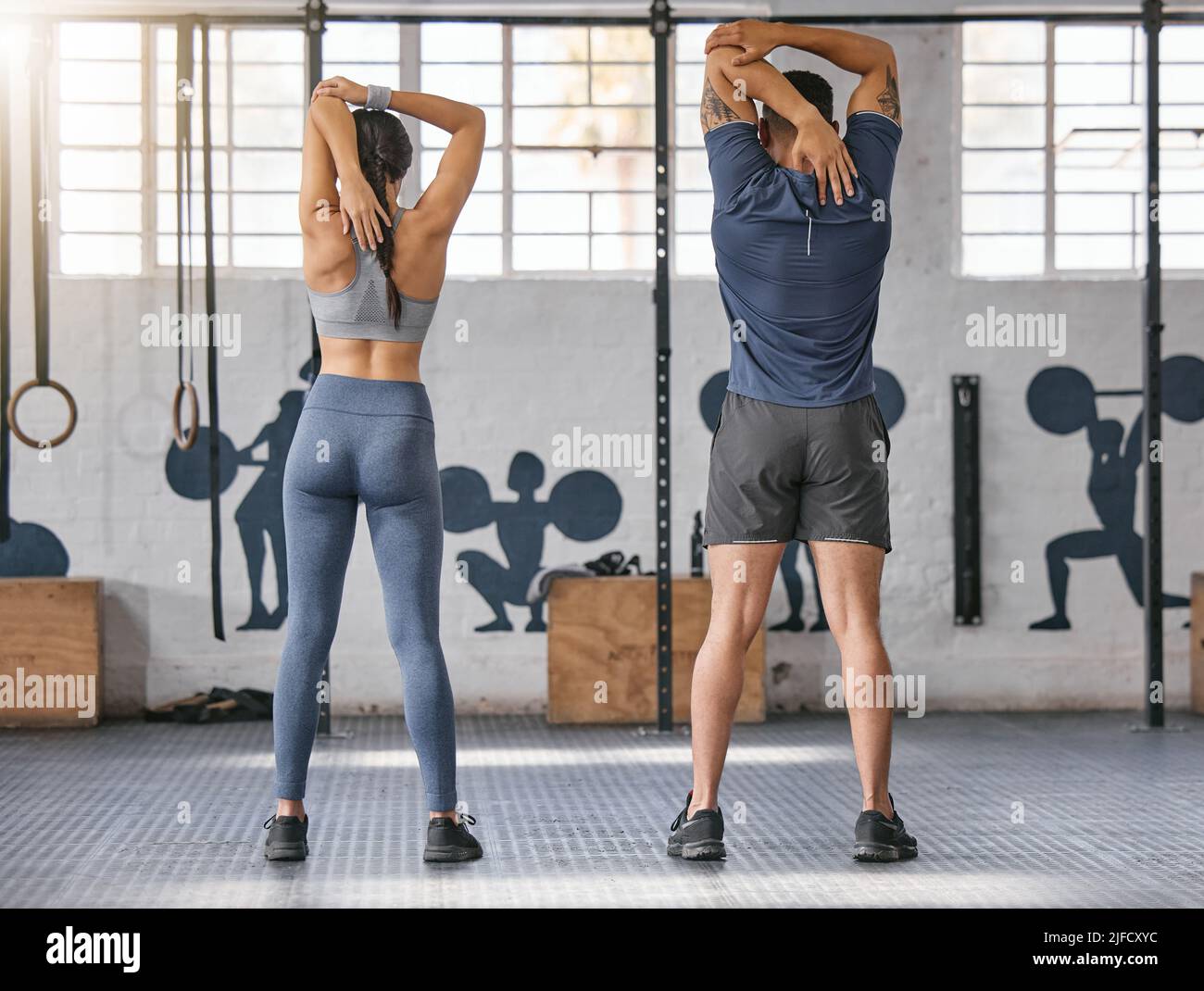 Two active caucasian athletes from behind behind stretching their arms and triceps by pulling elbow with hands towards spine behind head while Stock Photo