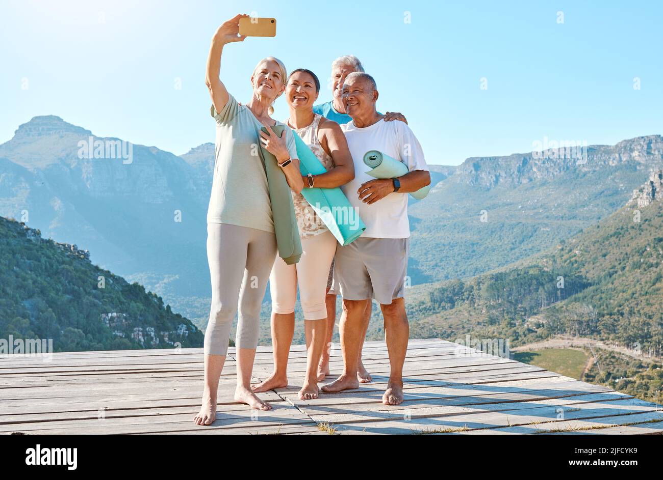 Group of active seniors posing together for a selfie or video call on a sunny day against a mountain view background. Happy diverse retirees taking Stock Photo