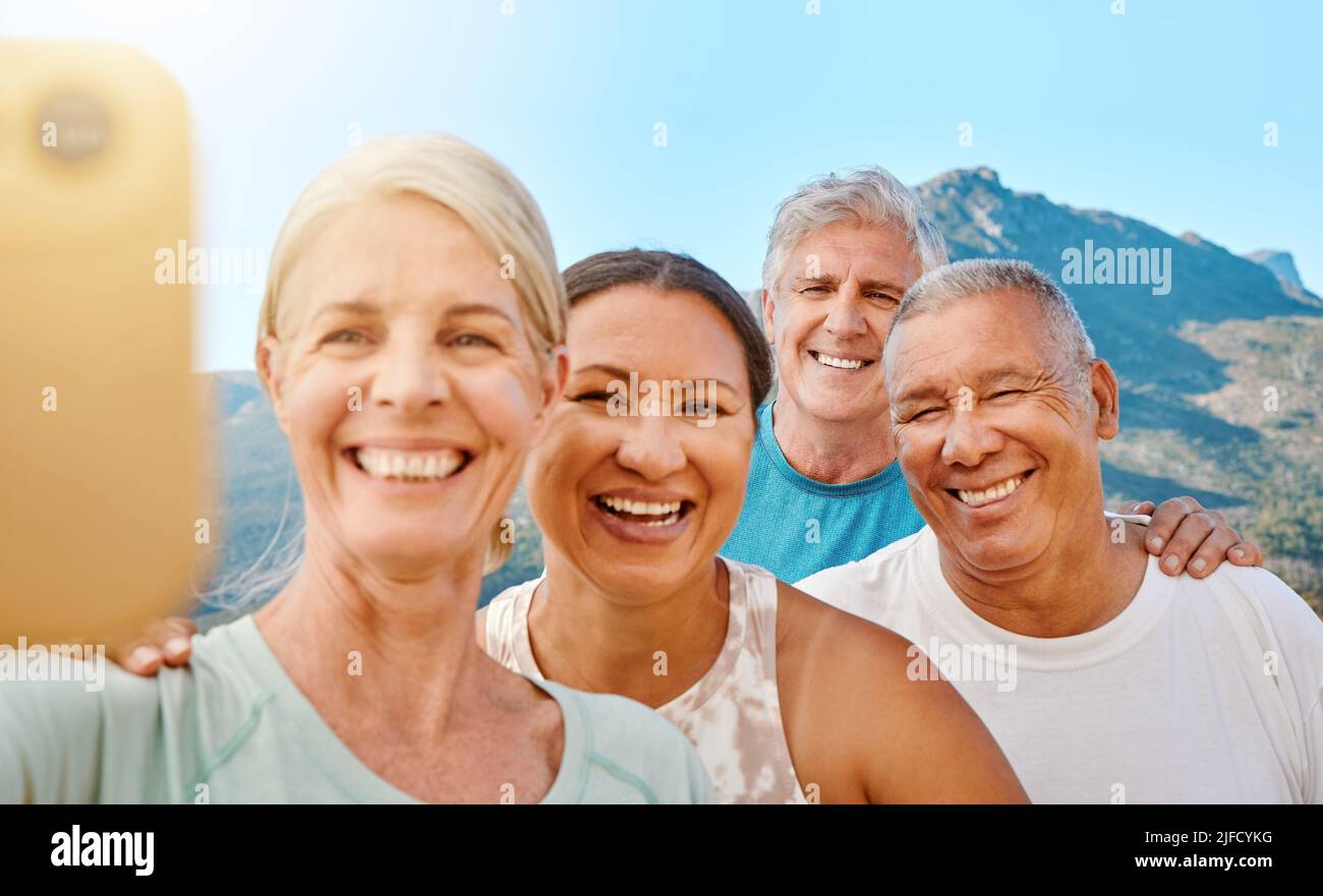 Group of active seniors posing together for a selfie or video call on a sunny day against a mountain view background. Happy retirees exercising Stock Photo