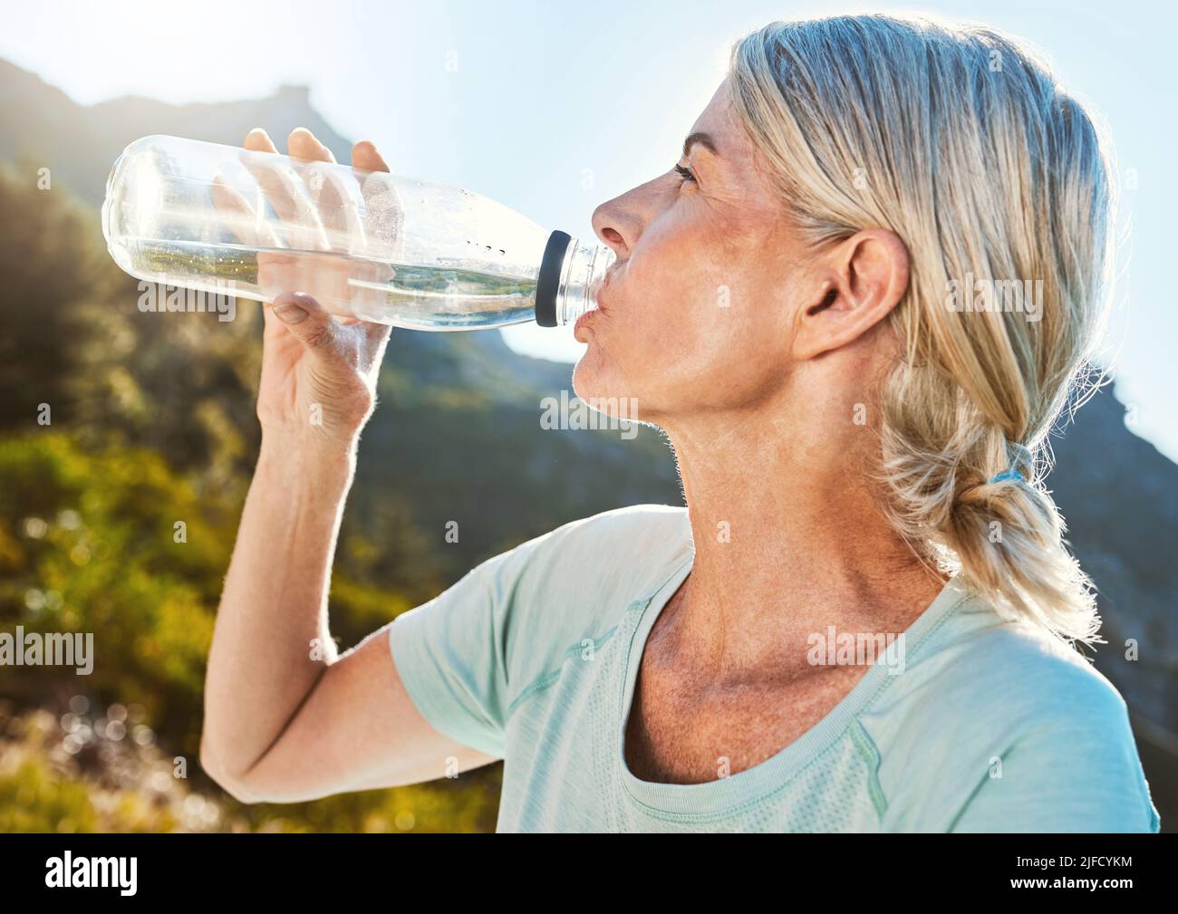 Active senior woman out for a run or jog in nature and drinking water while taking a break. Living active and healthy lifestyle Stock Photo