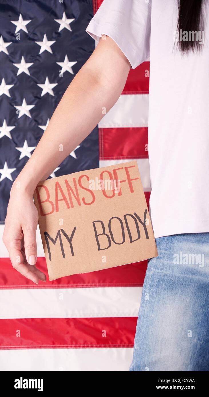 Woman holding a sign Bans Off My Body American flag on background. Protest against anti abortion law. Women's strike. Womens rights freedom. Stock Photo