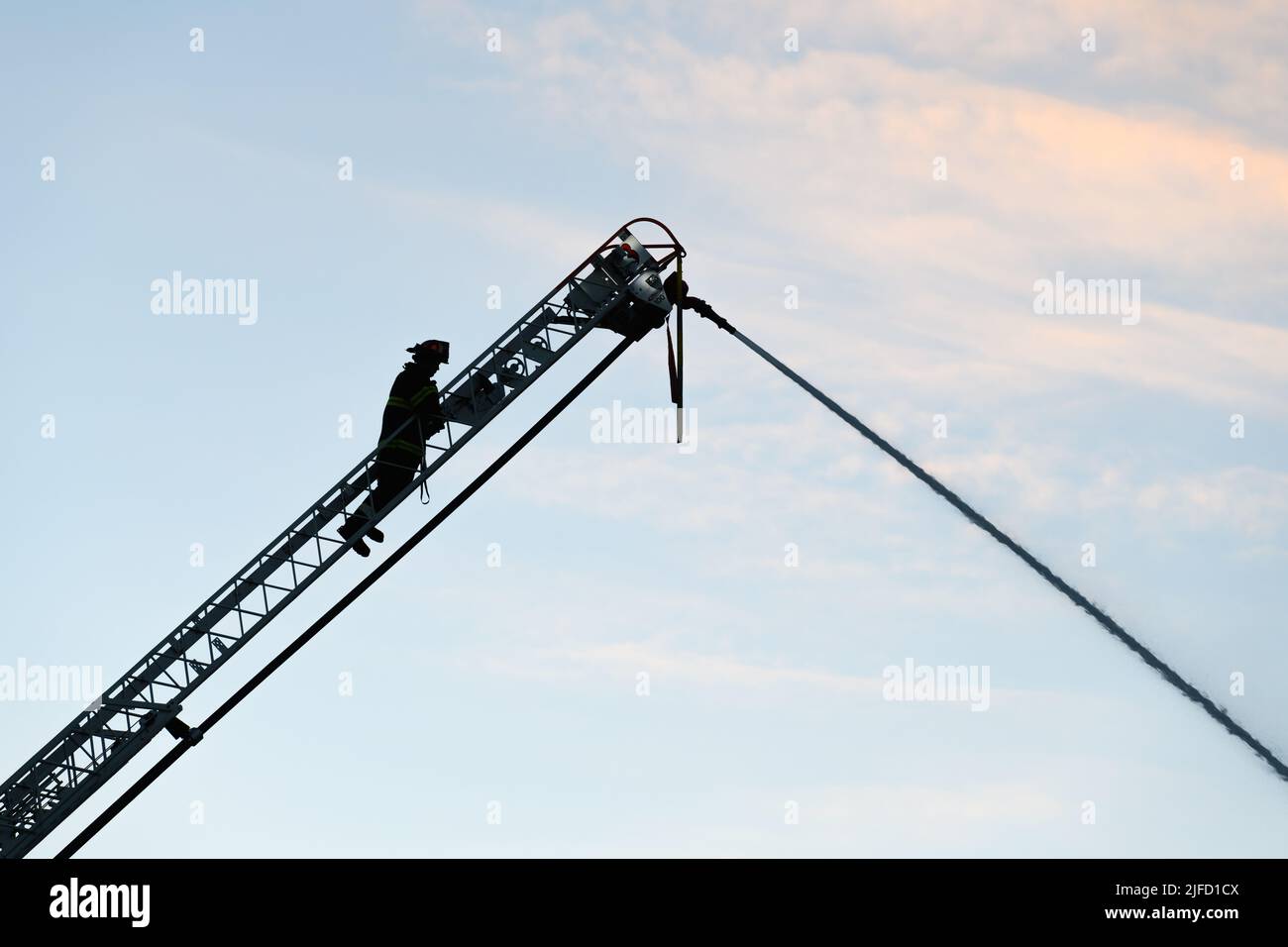 Seattle - June 30, 2022; Fire fighter on a ladder truck spraying stream of water in silhouette against a smokey moring sky Stock Photo