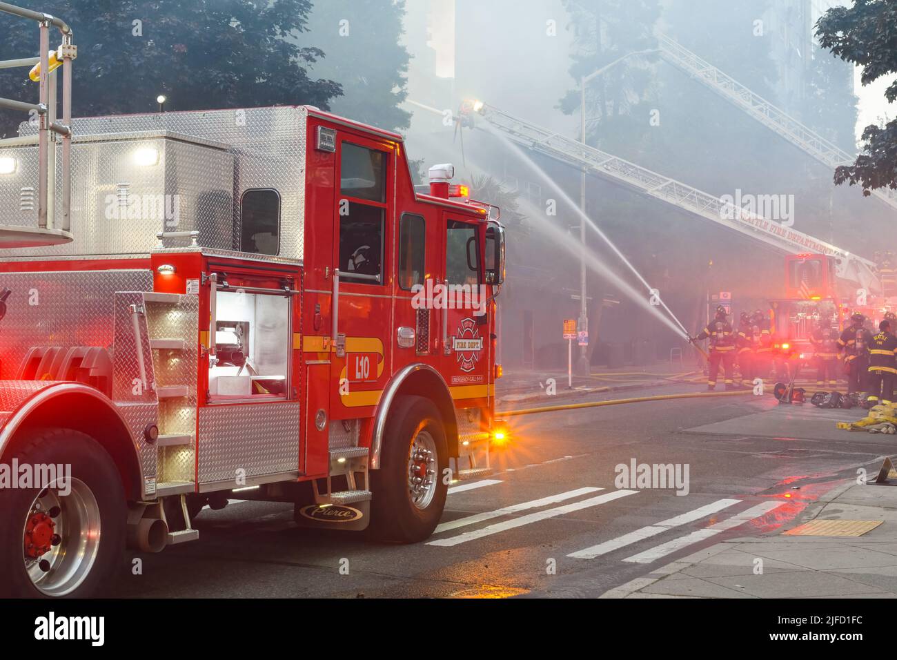 Seattle - June 30, 2022; Seattle fire department fighting an active fire in a smokey scene using ladder trucks and hoses with water streams Stock Photo