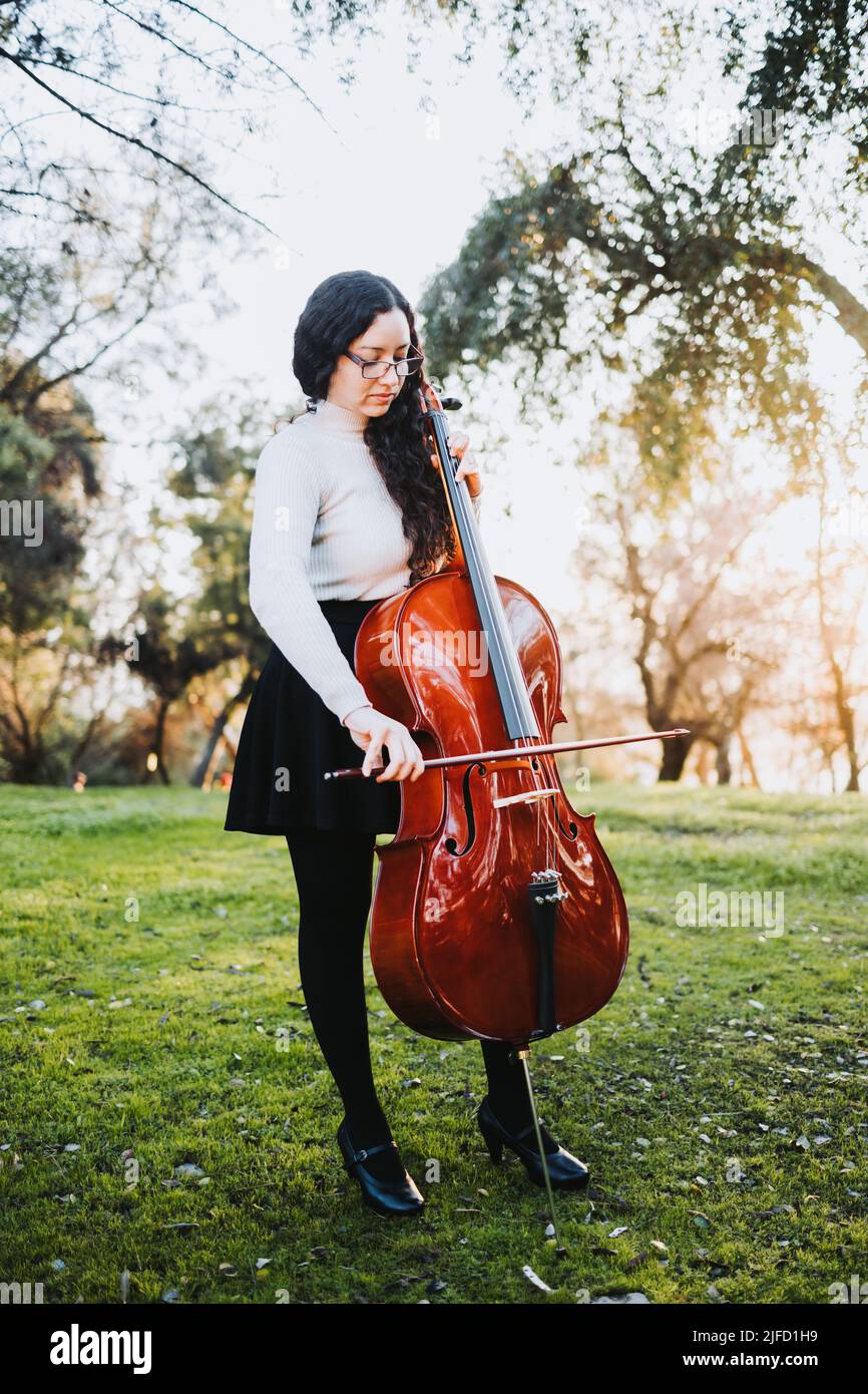 Young standing brunette woman with glasses playing cello at sunset in ...
