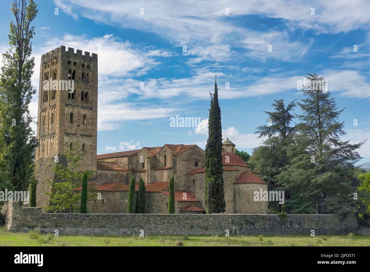 An abbey of Saint-Michel-de-Cuxa surrounded by growing trees under blue bright sky Stock Photo