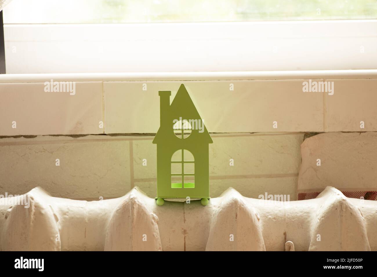 A small green house stands on an old cast-iron battery under the window in the apartment, a warm house, a heating installation Stock Photo