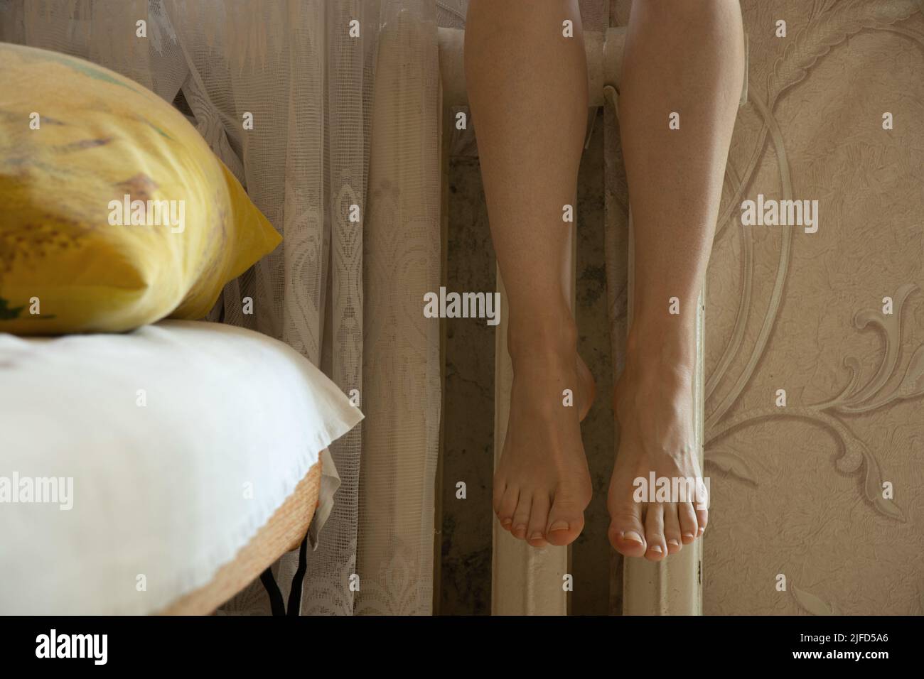 Women's feet on an old cast-iron battery in an apartment in winter, a cold apartment, a heating season, a battery in an apartment, it's cold Stock Photo
