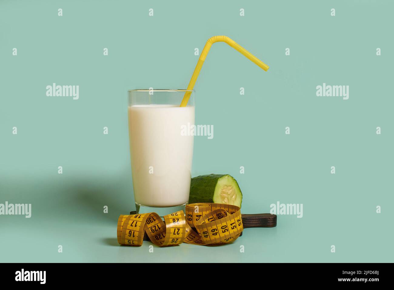A glass of milk with a plastic tube, a cucumber and a tailor's meter  Stock Photo