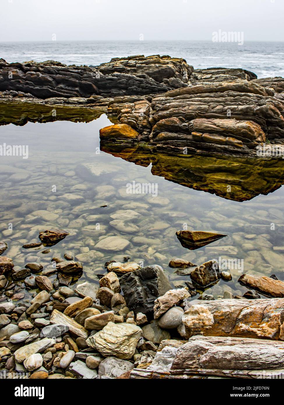 A calm clear rock pool between with pebbles at it’s the bottom, along the Tsitsikamma coast, South Africa, on a cold overcast morning Stock Photo