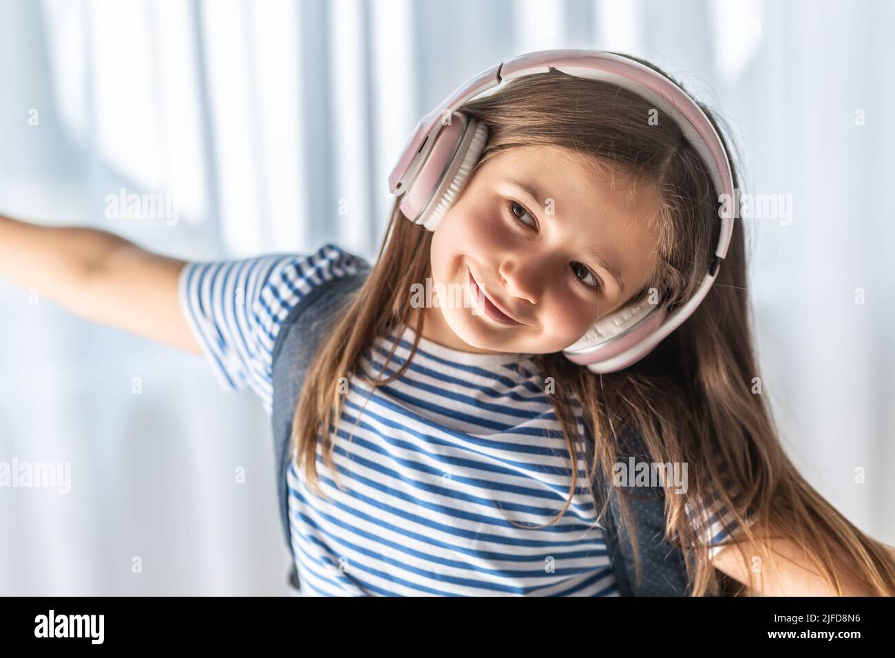Cute baby listens to music through wireless headphones, enjoys tunes and dances. Stock Photo