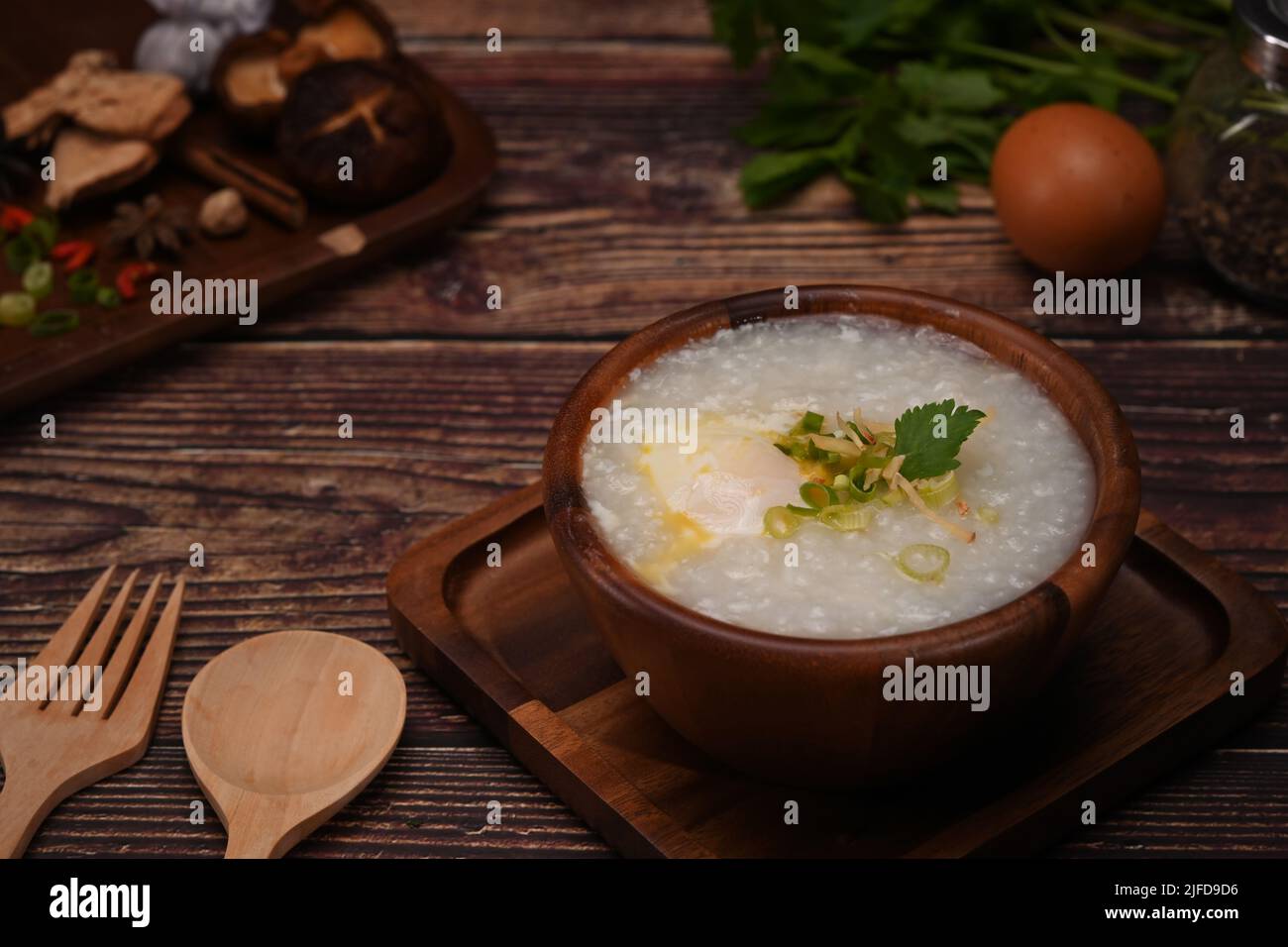 Rice porridge with boiled egg ,sliced ginger and slice scallion in bowl on wooden table. Traditional Chinese breakfast Stock Photo