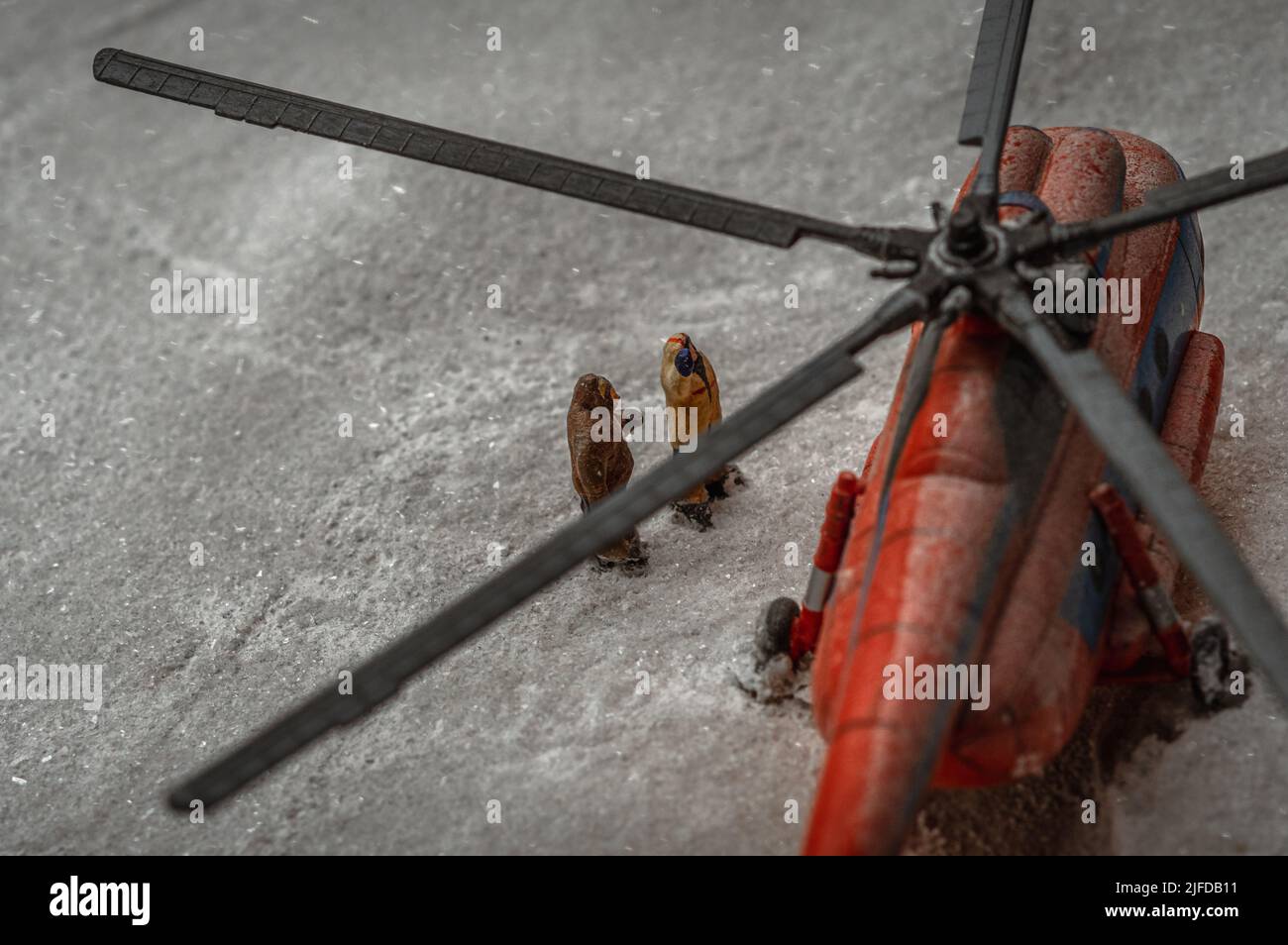 Toy representation of a red helicopter and two pilots in jumpsuits amid the snowstorm. Stock Photo