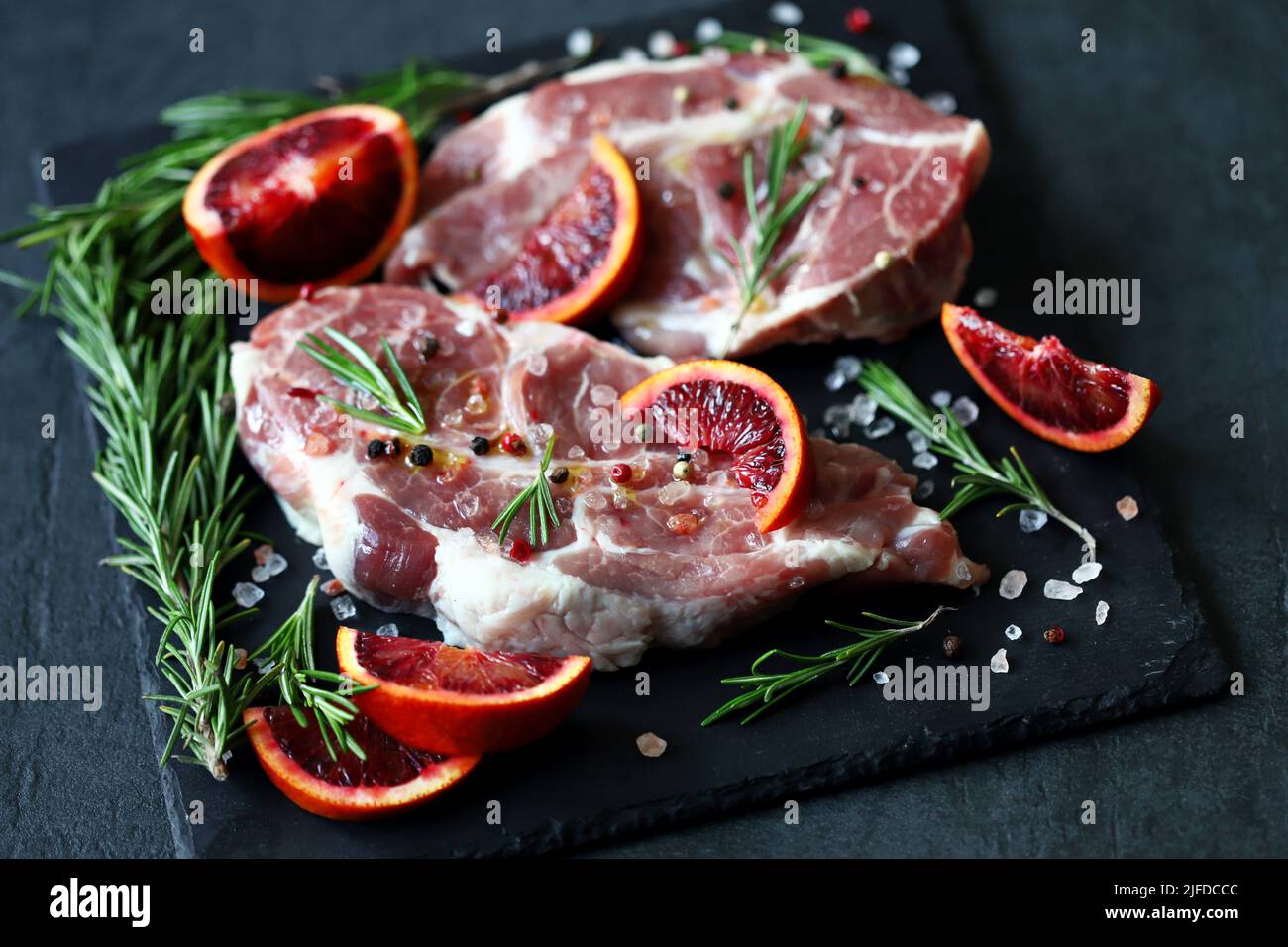 Raw pork steaks with rosemary and orange marinated on a stone board. Cooking meat steaks. Stock Photo