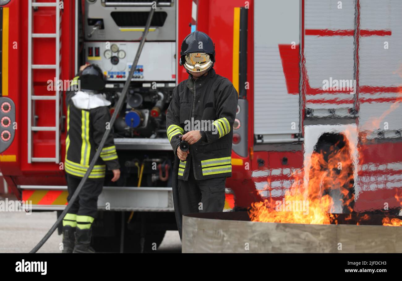 firefighters drill with a real fire and fire truck in the background Stock Photo