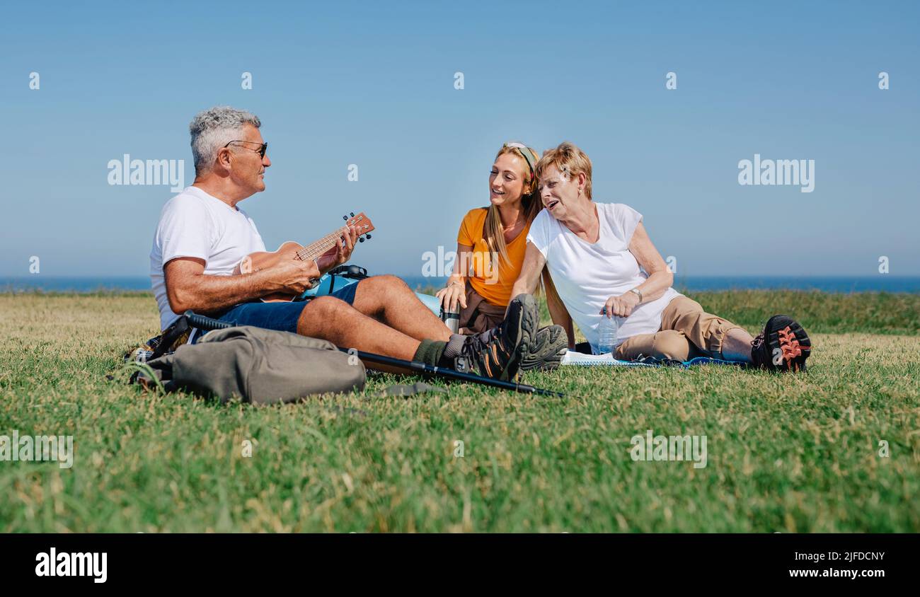 Adult family playing ukulele and singing sitting on a blanket during an excursion Stock Photo