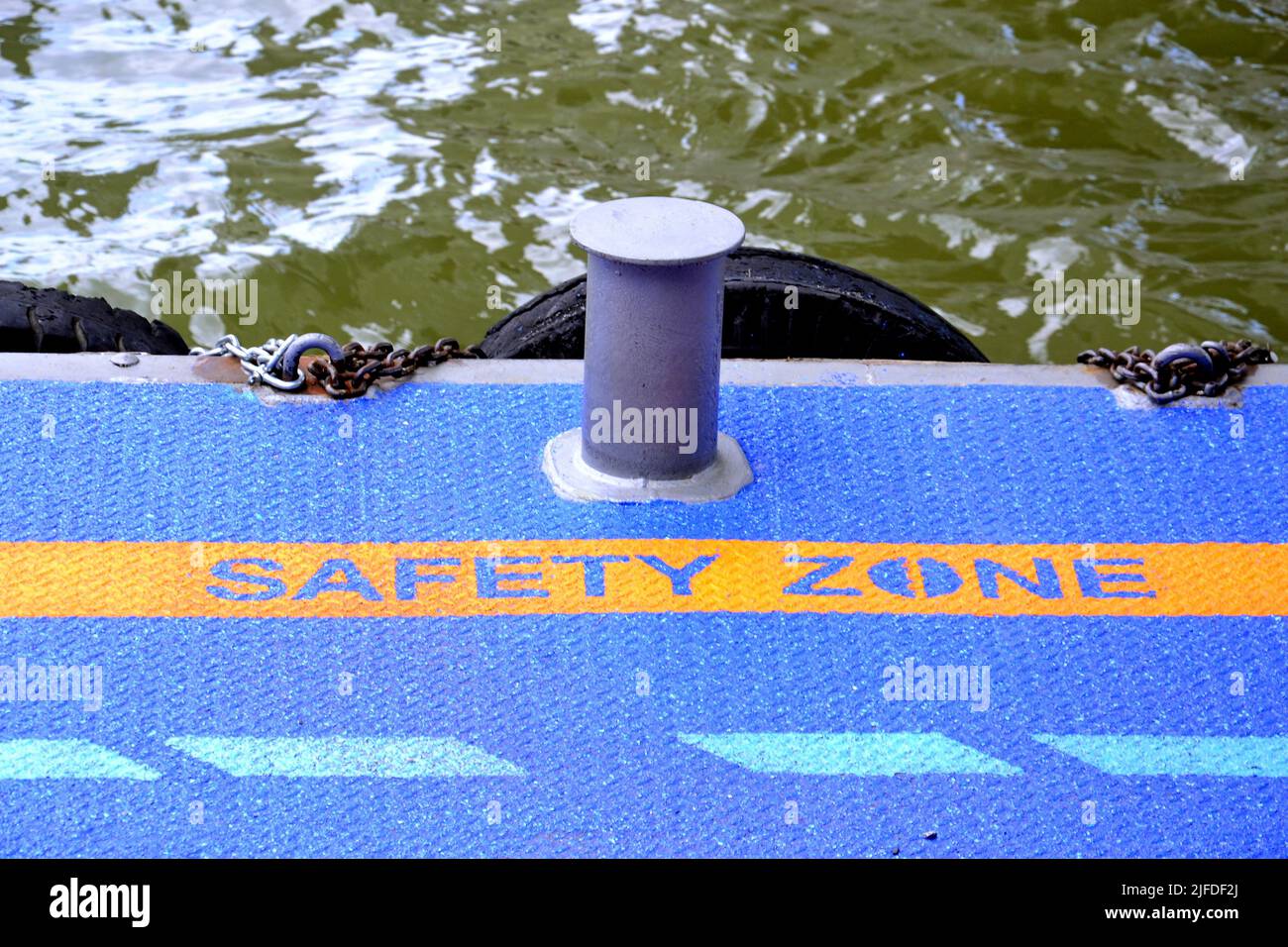 SAFETY ZONE sign instructs passengers to keep clear at a quayside with tyres hanging into the water to act as a buffer for boats. Stock Photo