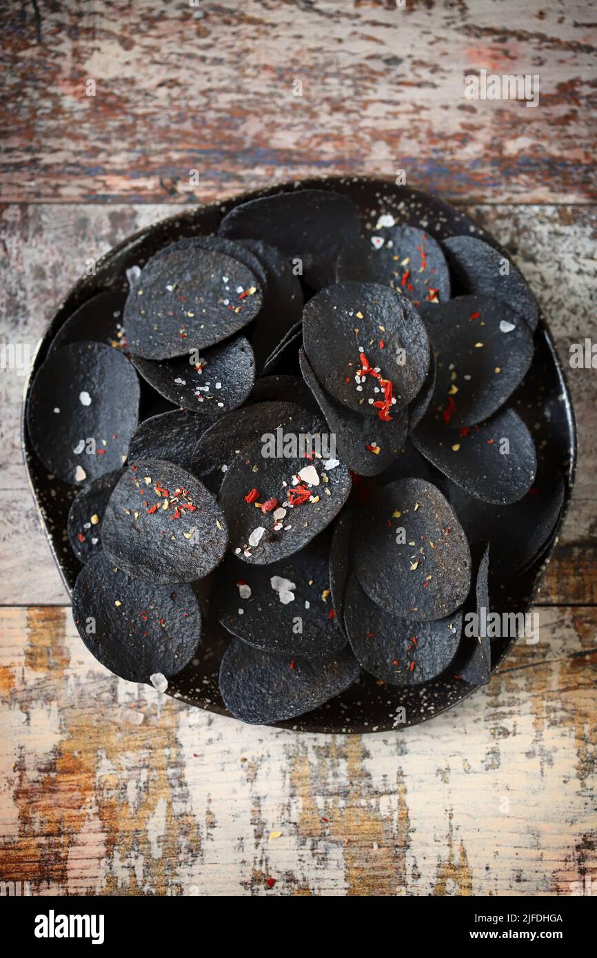 Black food. Black chips with spices on a plate. Black food trend. Cuttlefish ink food. Stock Photo