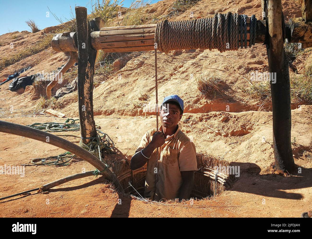 Ilakaka, Madagascar - April 30, 2019: Unknown Malagasy man standing in ground precious stone mine hole or well, half body visible, holding rope - abou Stock Photo