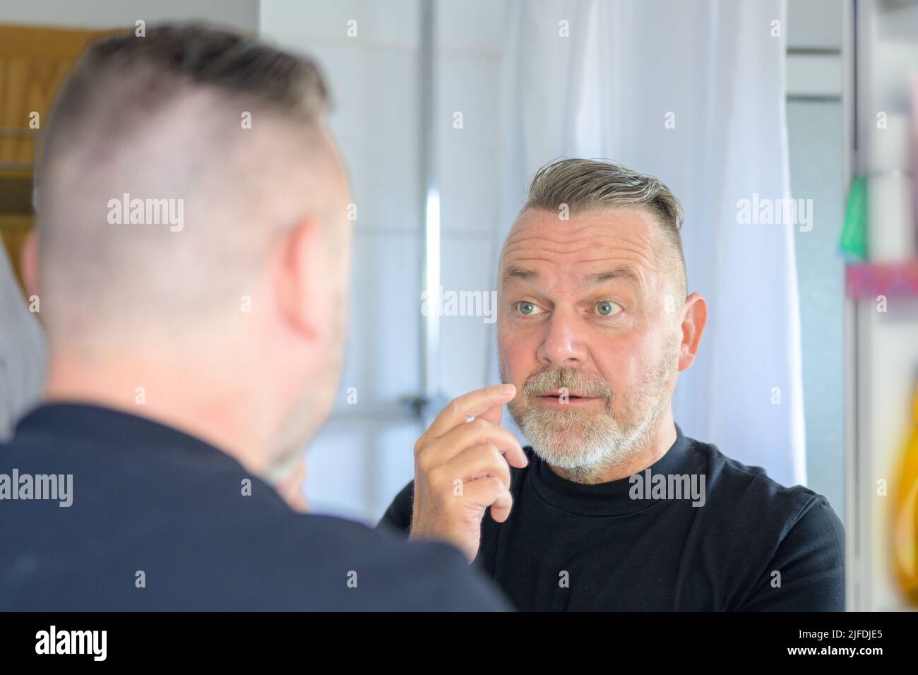 Dismayed middle-aged man looking at the fleshy bags under his eyes with a view to his reflection in the mirror Stock Photo
