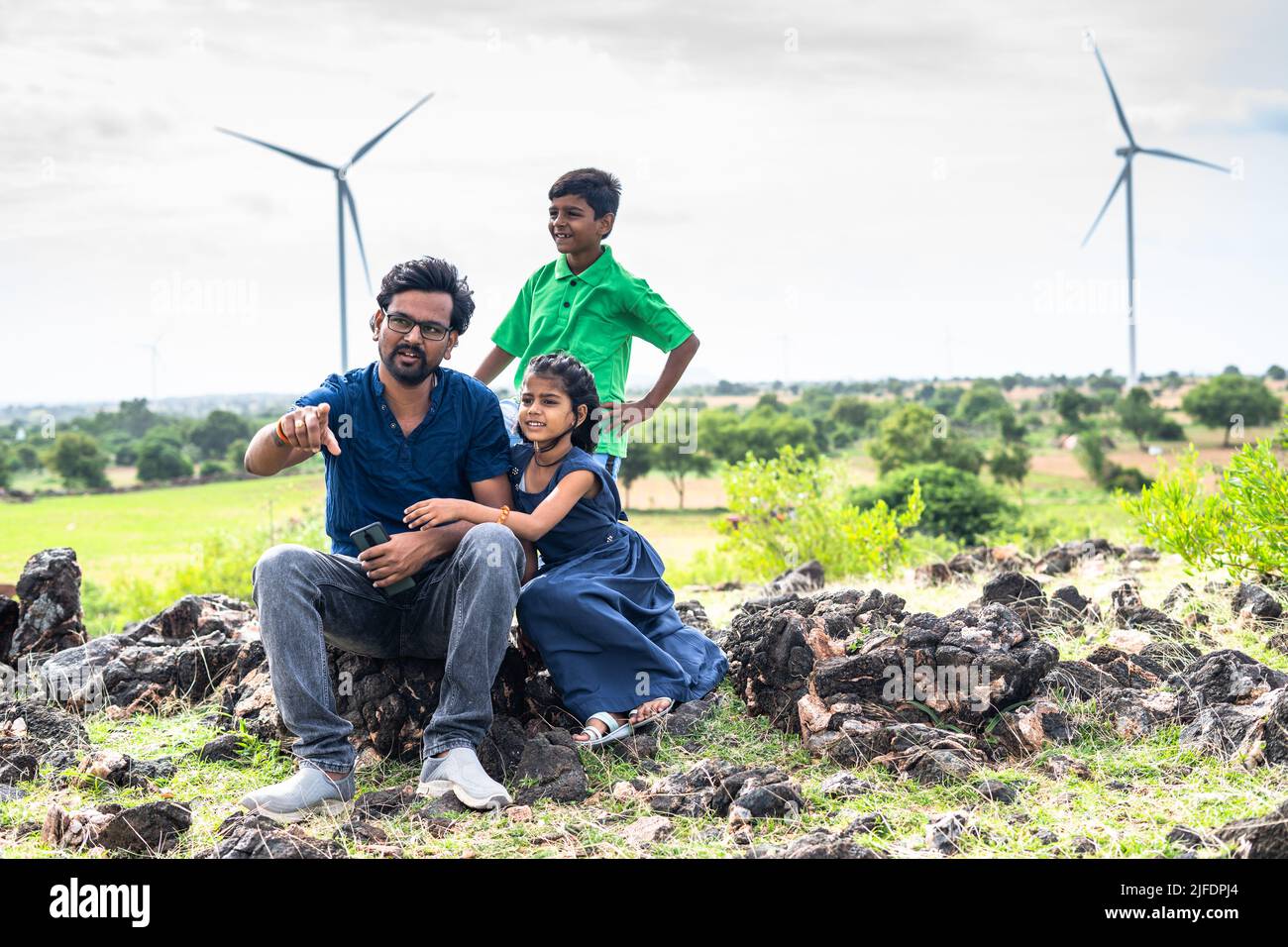 Happy smiling father with kids on top of mountain near wind power fans having good time - concept of exploration, sustainable lifestyles and bonding Stock Photo