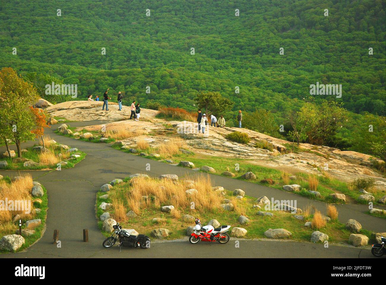 A group of people walk from their motorcycles to get a view near the cliff in New York's Bear Mountain and enjoy the views of the woodlands and forest Stock Photo