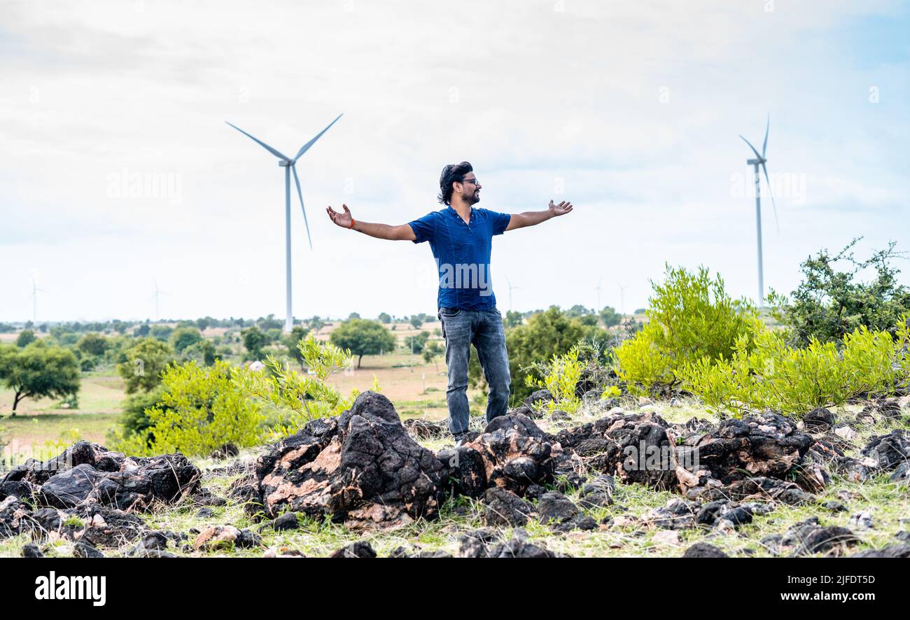 man feeling nature fresh air by stretching arms at wind turbine near - concept of sustainable lifestyle, freedom and relaxation Stock Photo