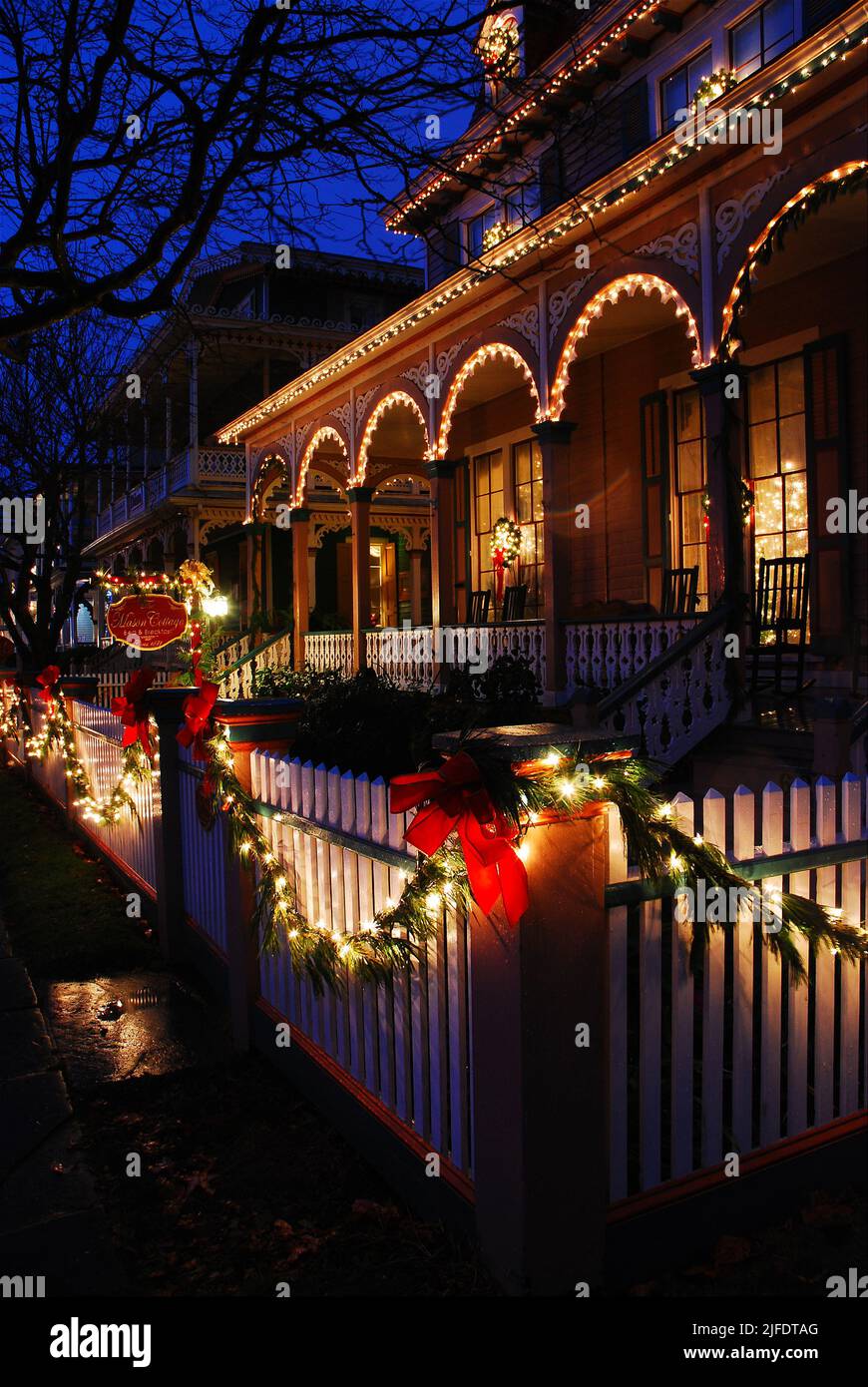 A beautiful Victorian house is decorated with holly and lights along a white picket fence at Christmas in Cape May on the New Jersey Shore Stock Photo