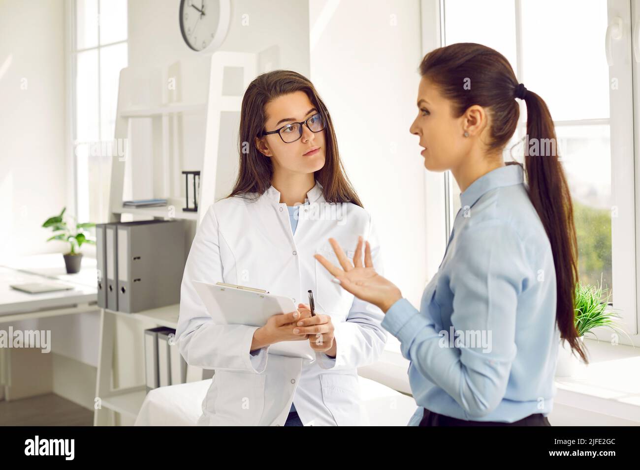 Young Caucasian woman in nurse coat works as doctor in cosmetology clinic listens to female patient Stock Photo