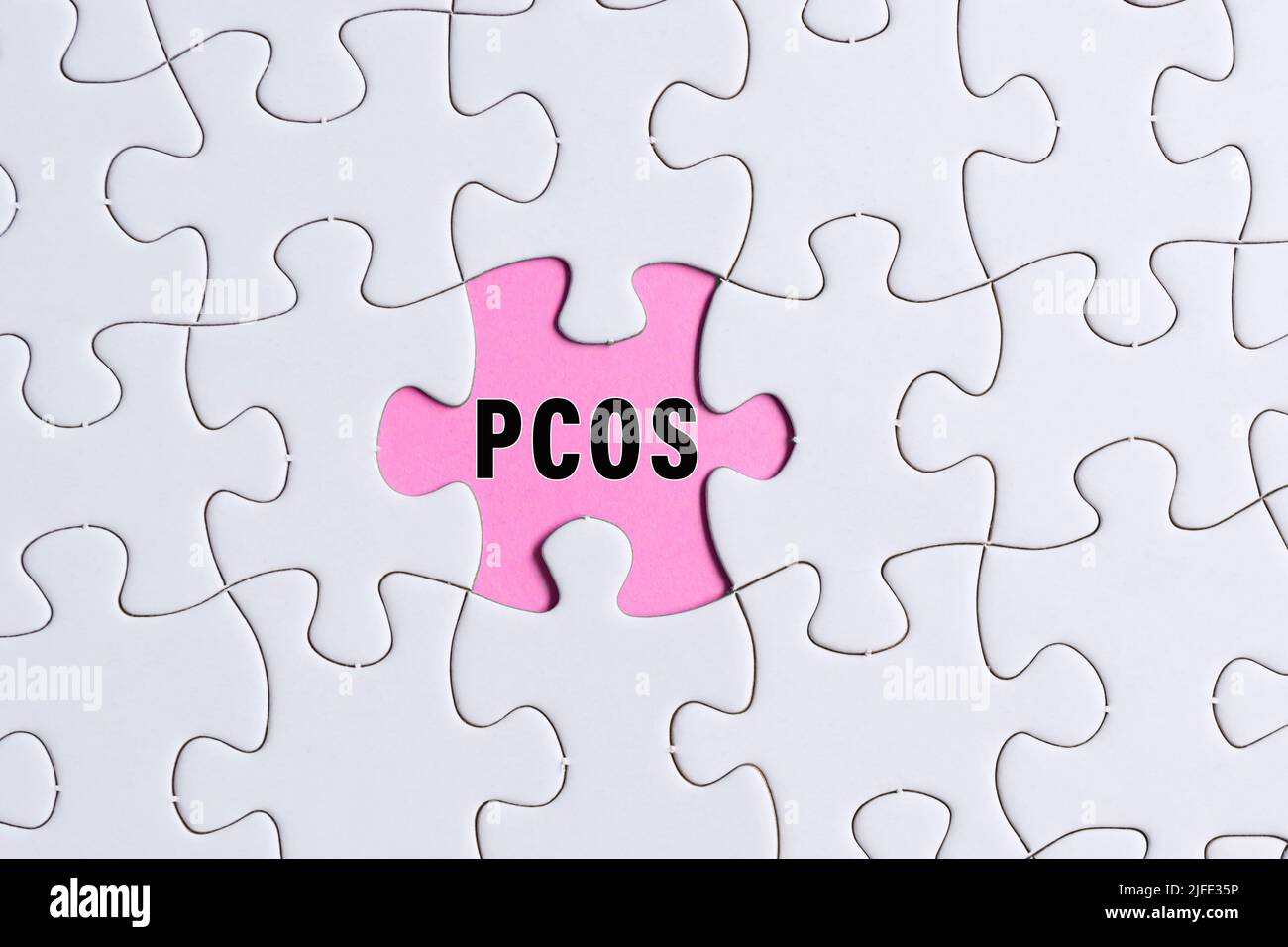 PCOS text on white jigsaw puzzle over pink background. Polycystic Ovary Syndrome Health Care concept. Stock Photo
