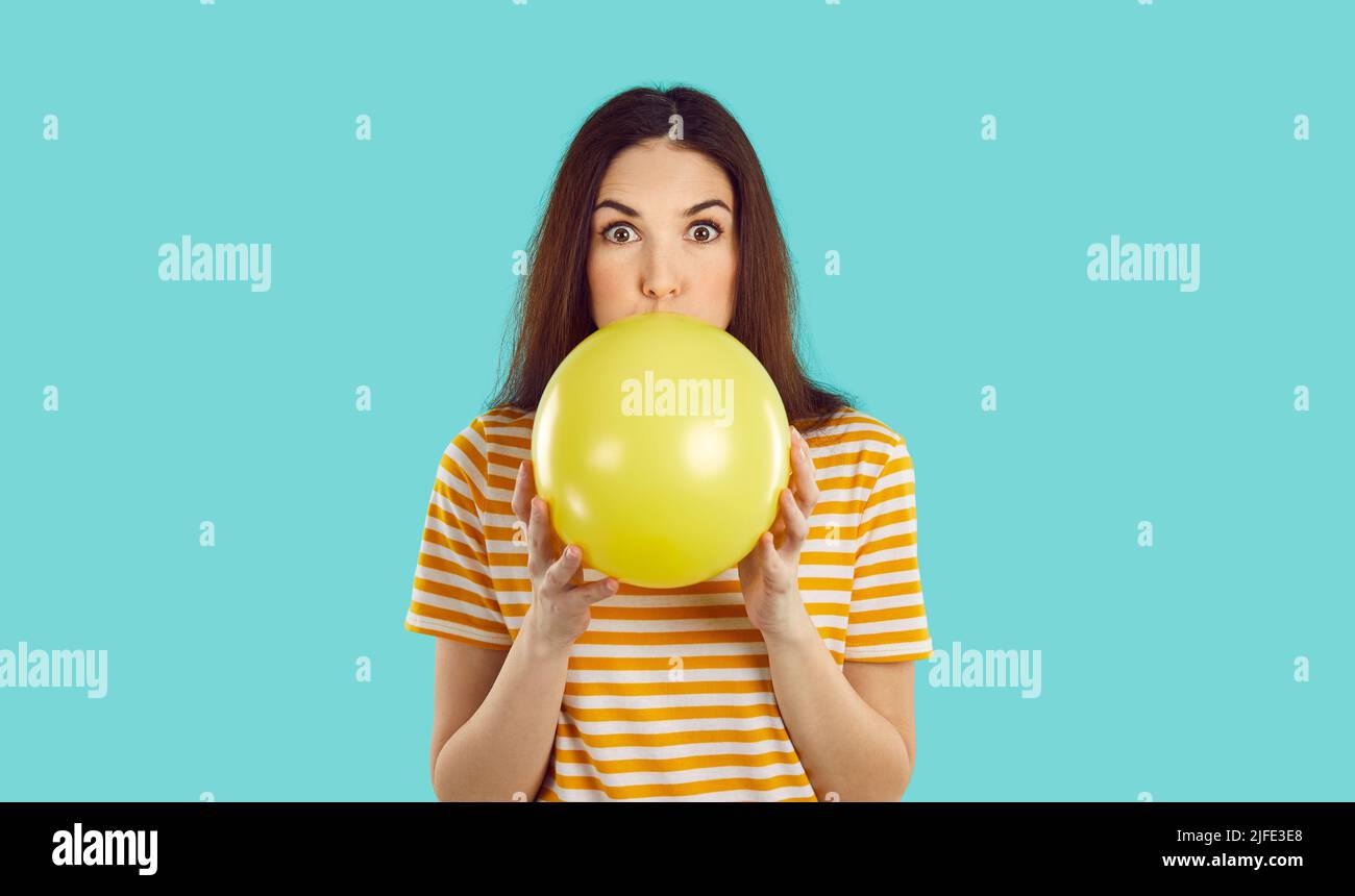 Funny woman isolated on turquoise background inflating yellow balloon for birthday party Stock Photo