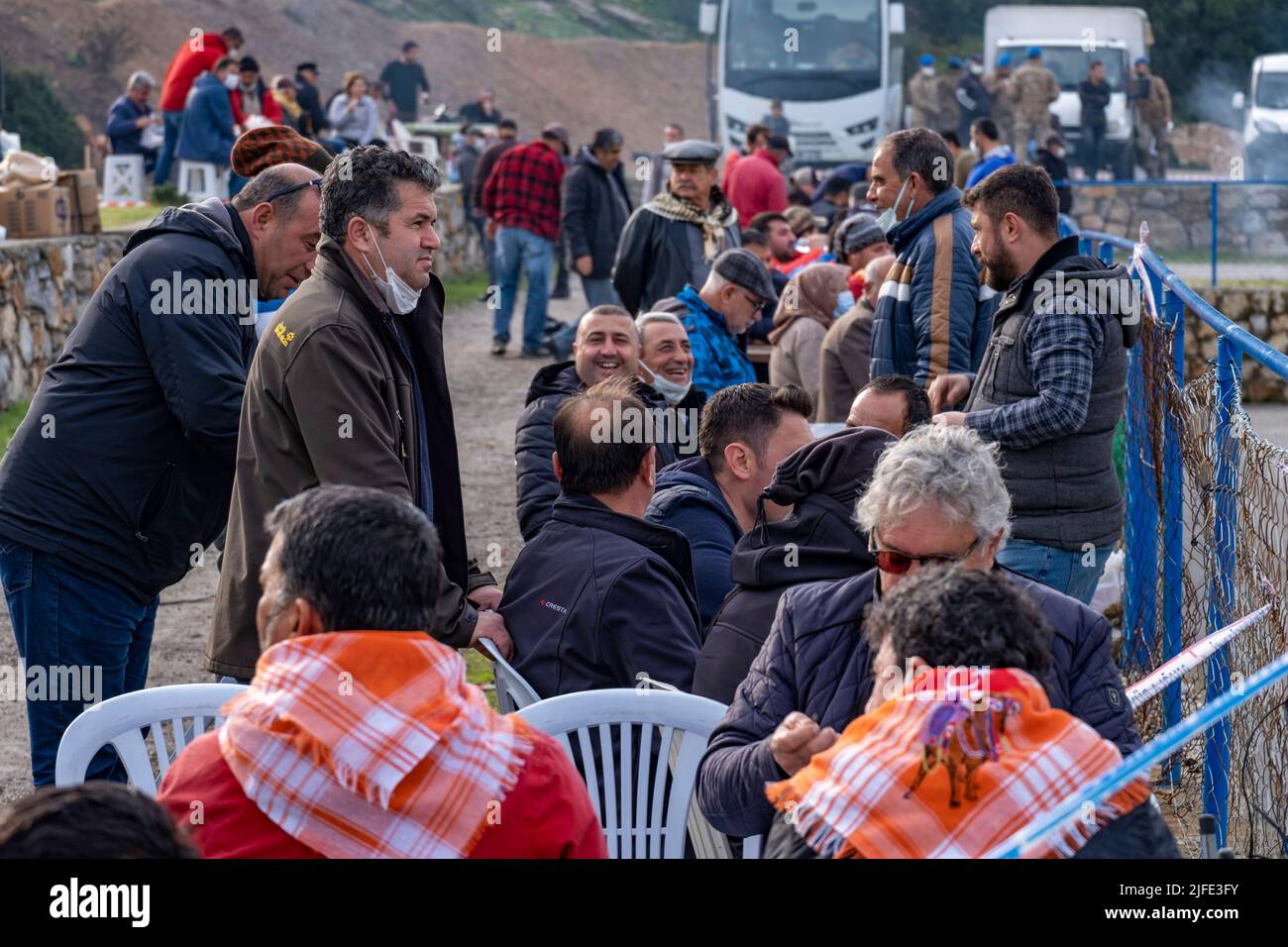 Bodrum, Turkey - 8th Jan. 2022: Local people chatting, laughing at the traditional outdoor camel wrestling fight. Some men using face mask Stock Photo
