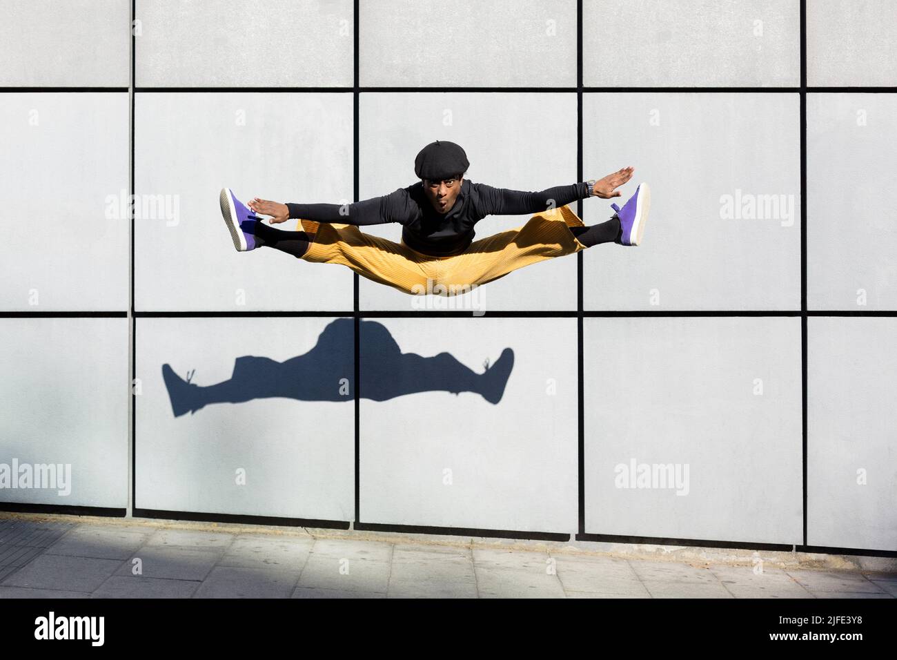 African American young adult man jumping energetically in the street. Dancer doing acrobatics in the city. Modern look, aesthetics Urban lifestyle. Sp Stock Photo