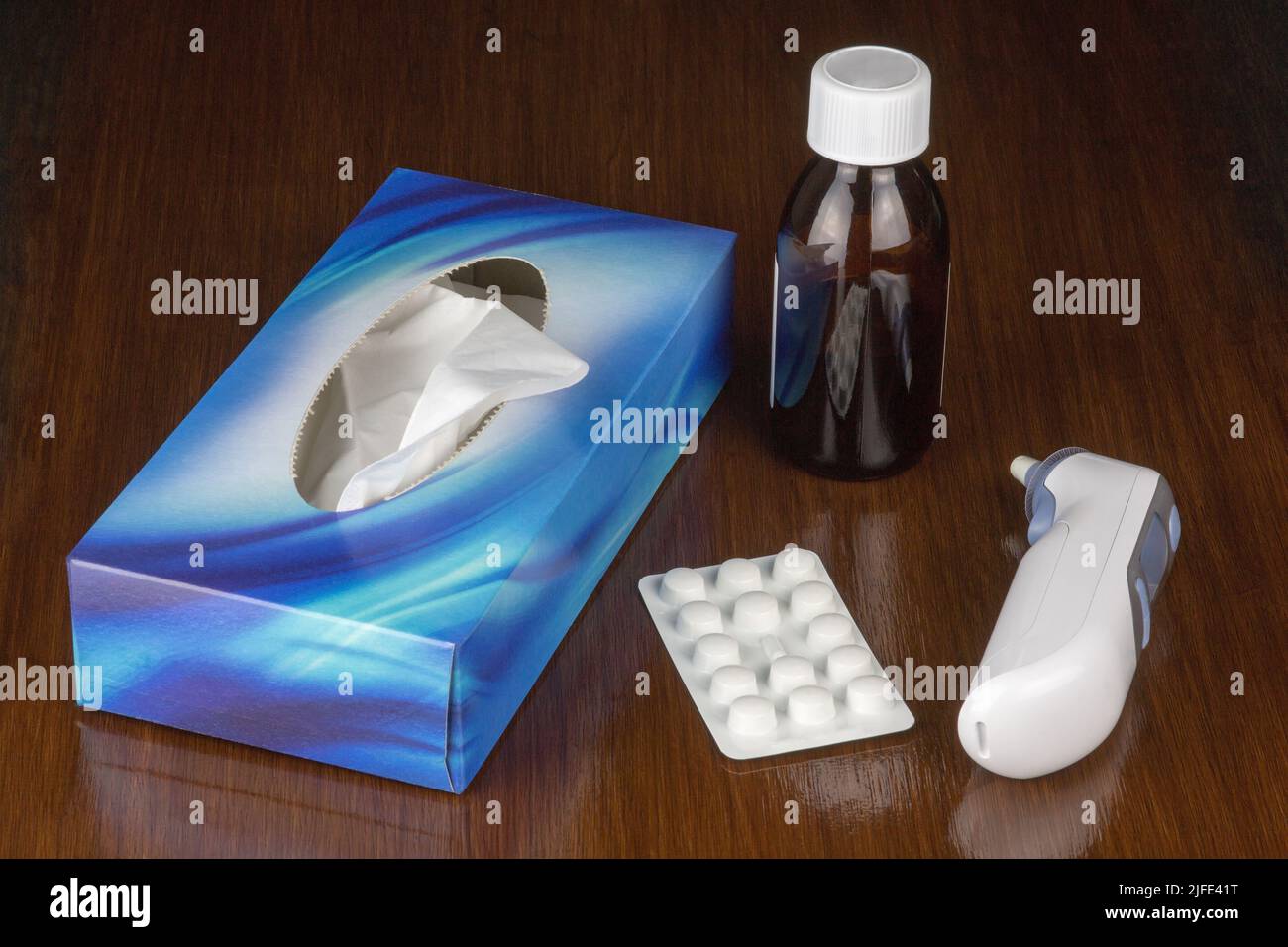 Medicine bottle with box of tissues thermometer and tablets on a polished table surface Stock Photo