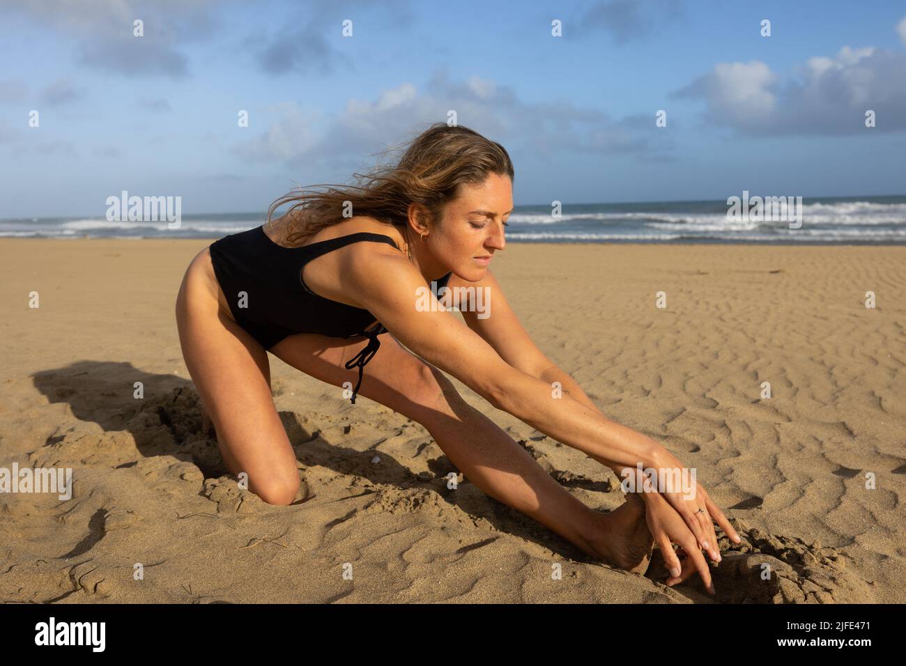 German woman performing stretching exercises on the beach. Stock Photo