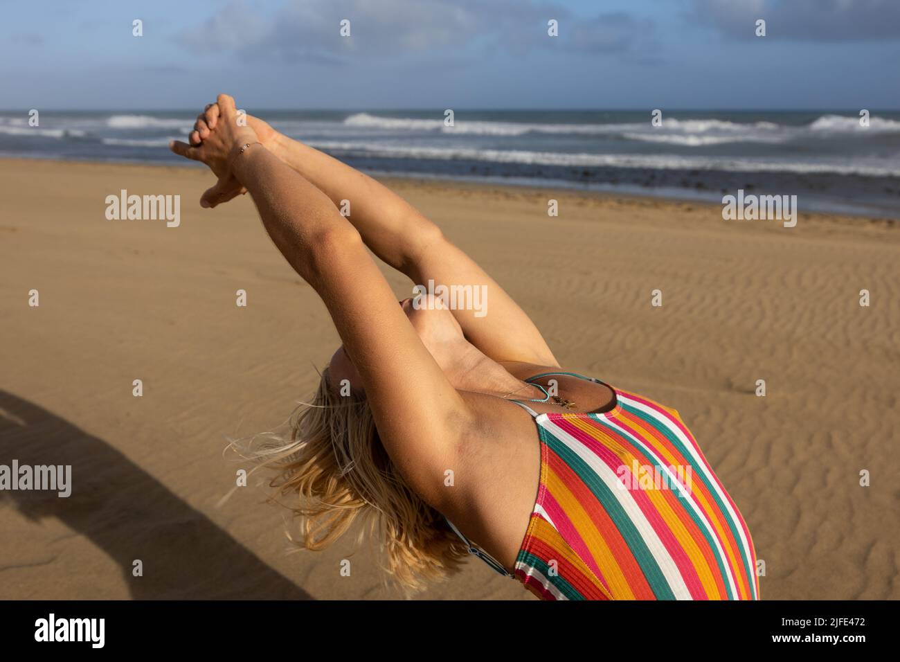 German woman performing stretching exercises on the beach. Stock Photo