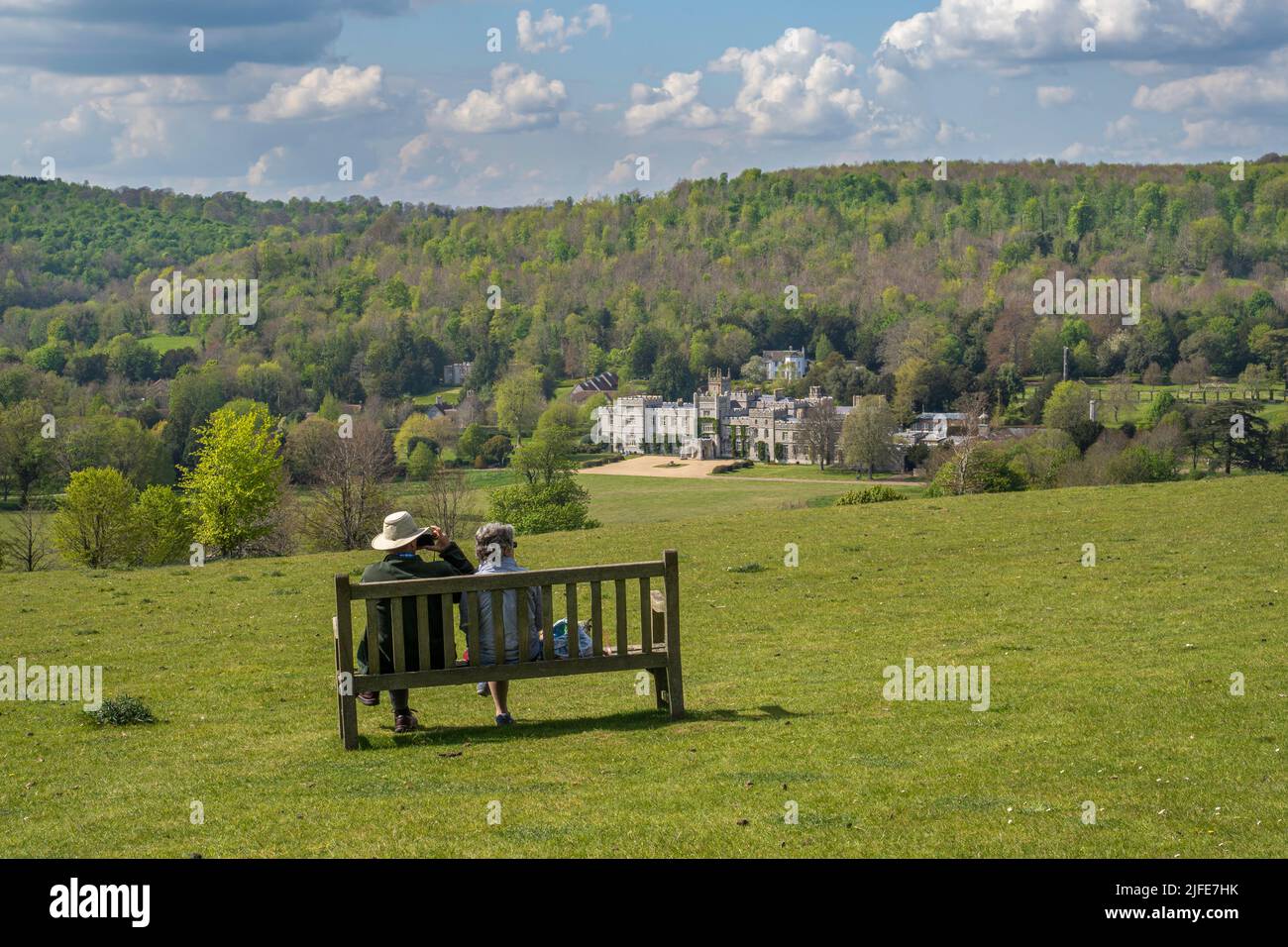 Two people sitting on a bench and admiring the view from the South Downs looking down onto West Dean College Stock Photo