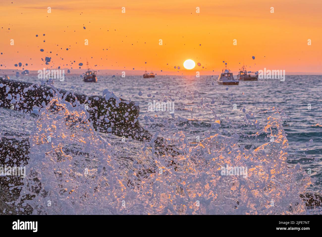 Selsey sunrise between the fishing boats with illuminated spray hitting the shore Stock Photo