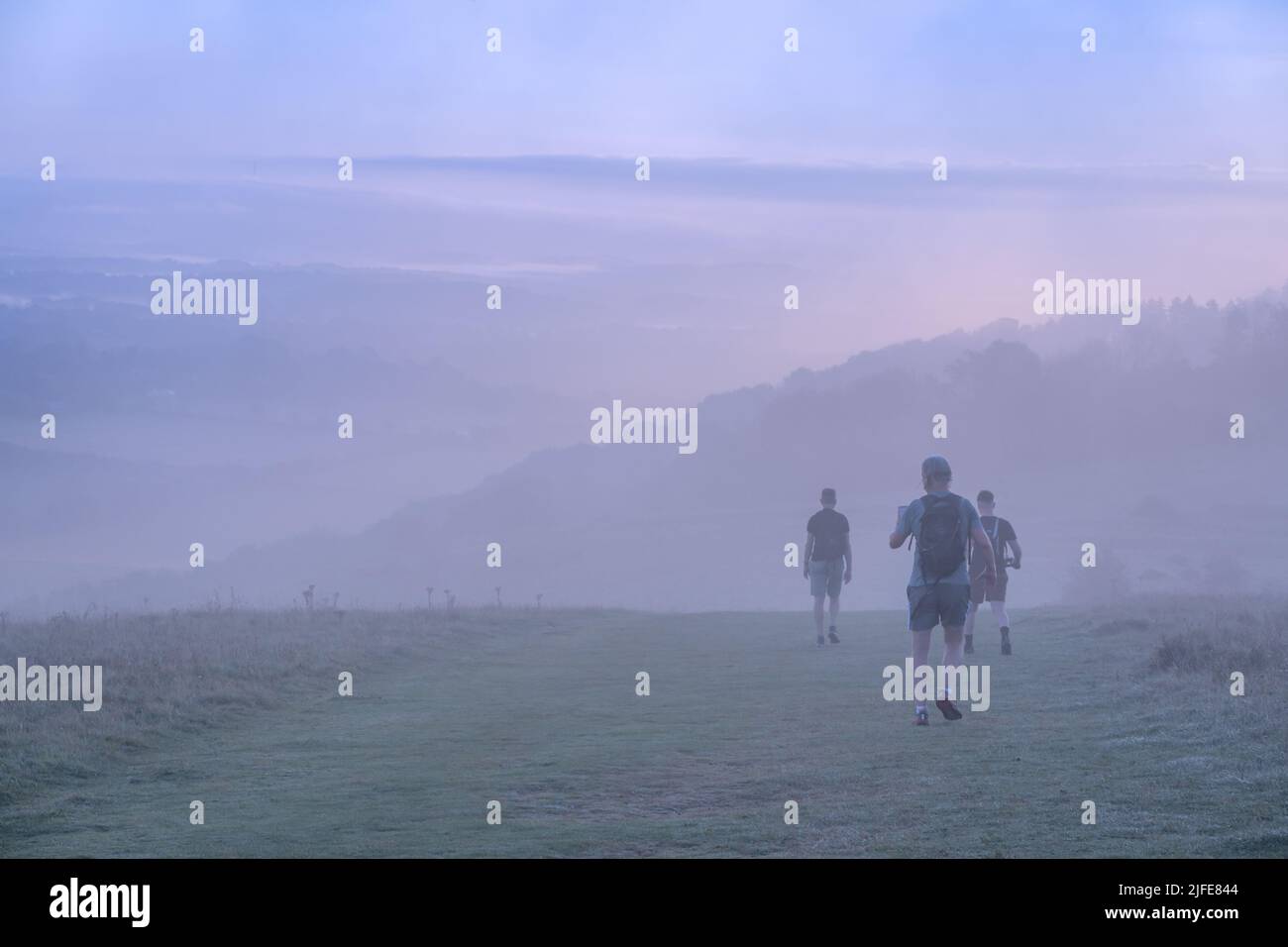 Early morning joggers on Harting Hill on the South Downs, disappear down in to the mist as the sun rises at the start of a new day. Stock Photo