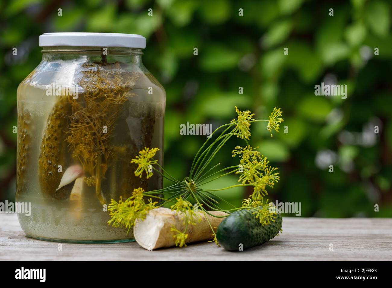 Pickles in a jar on an old wooden table in the garden. A summer sunny day. Cucumber, herbs, dill. Background image, copy space, horizontal. Eye Level Stock Photo