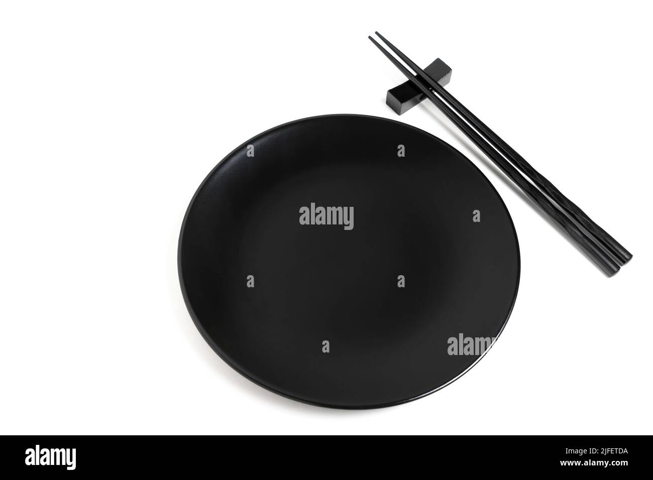 Pair of black lacquered chopsticks placed by a black plate isolated on